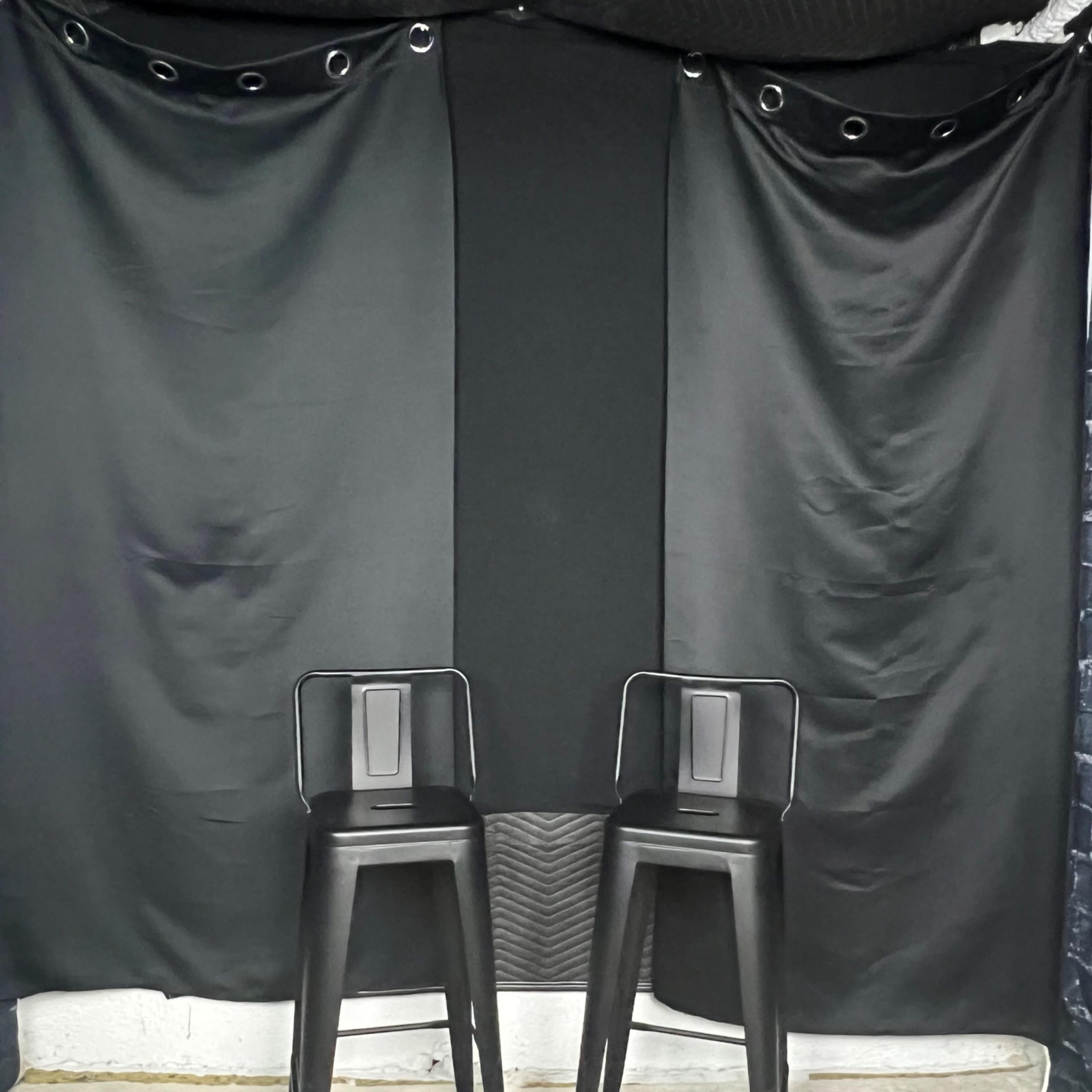 Two black bar stools are positioned in front of a black backdrop with draped fabric.