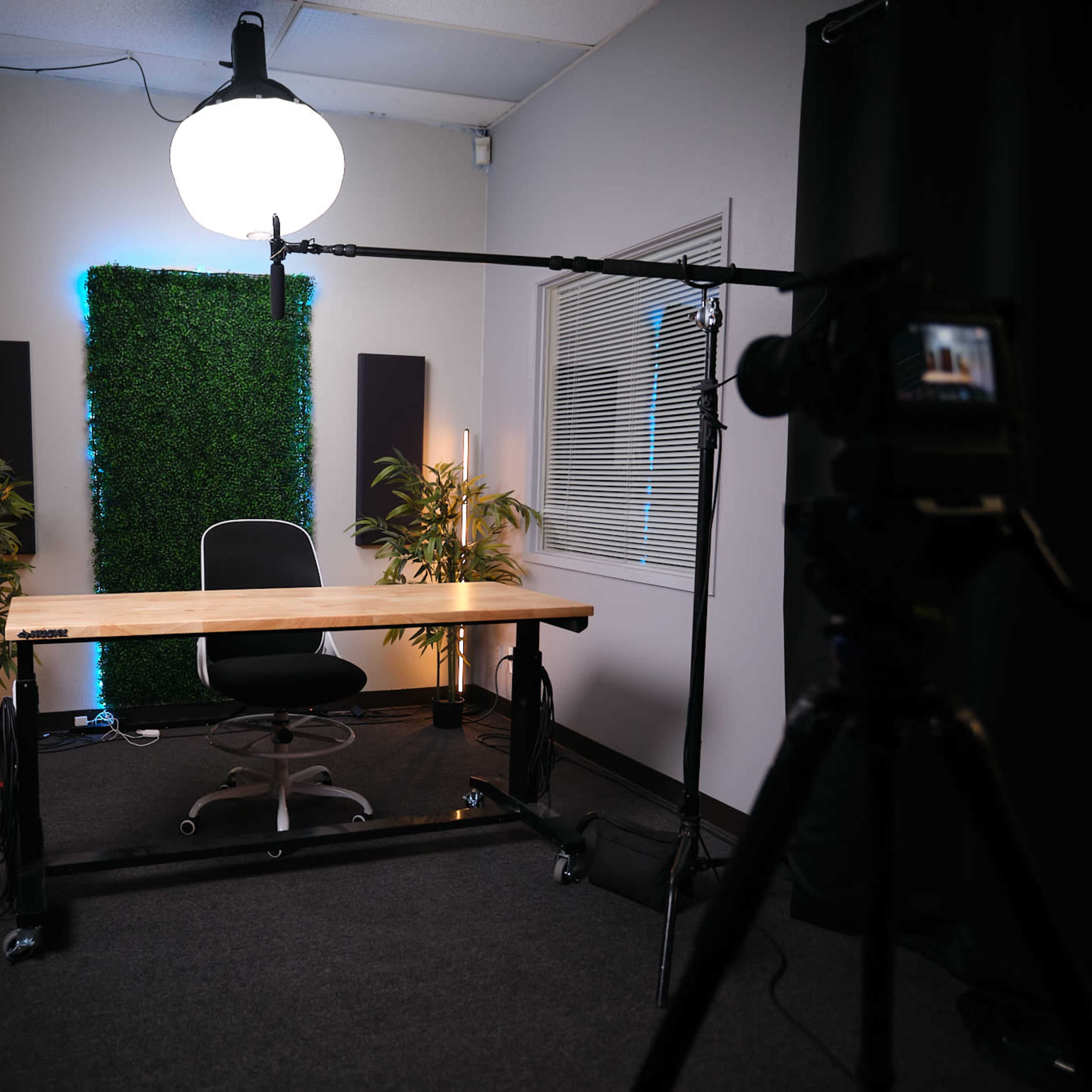 A cozy interview setup featuring two blue chairs, a small table with decorative items, and plants, all under soft, colored lighting.
