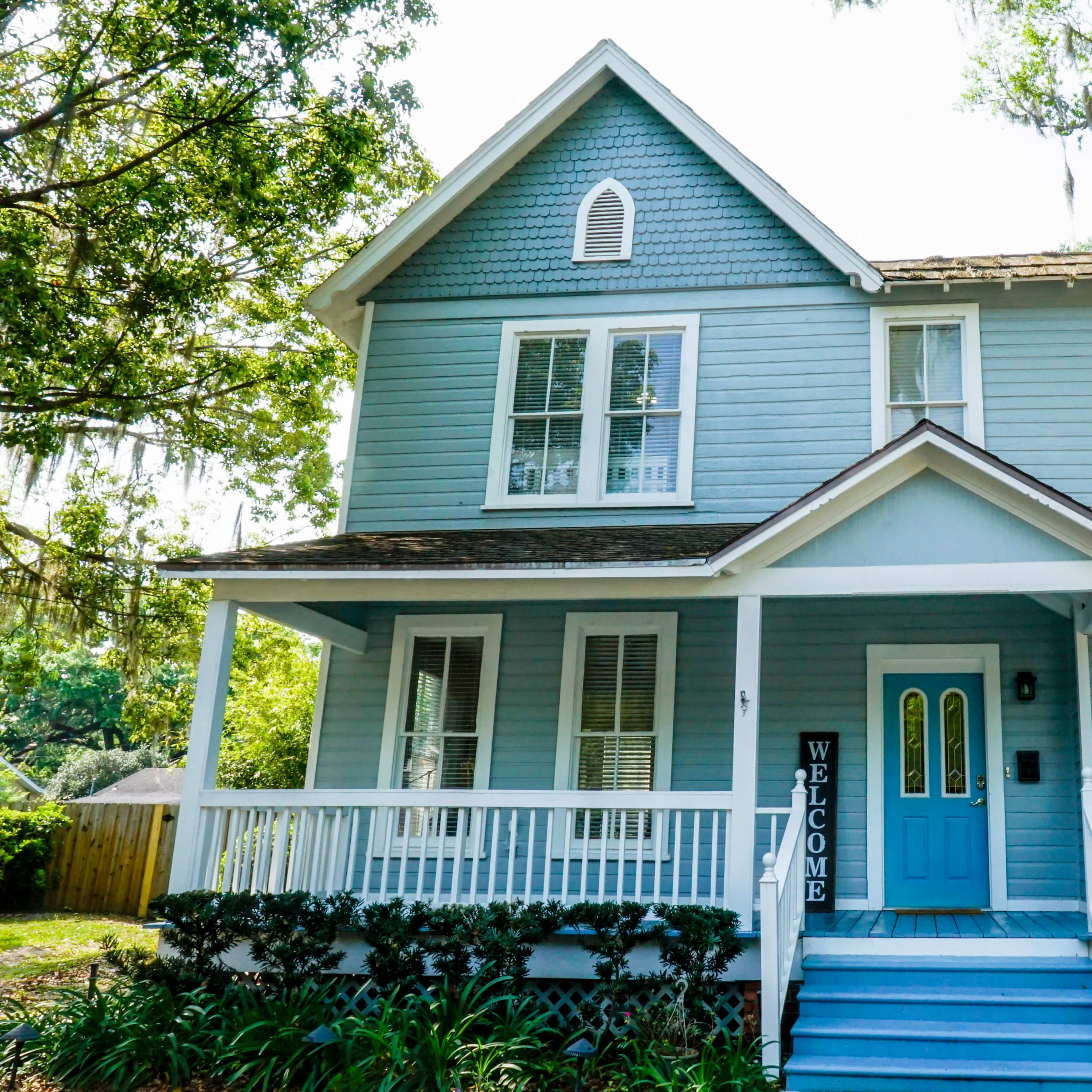 A blue two-story house with a welcoming front porch and a light blue door.