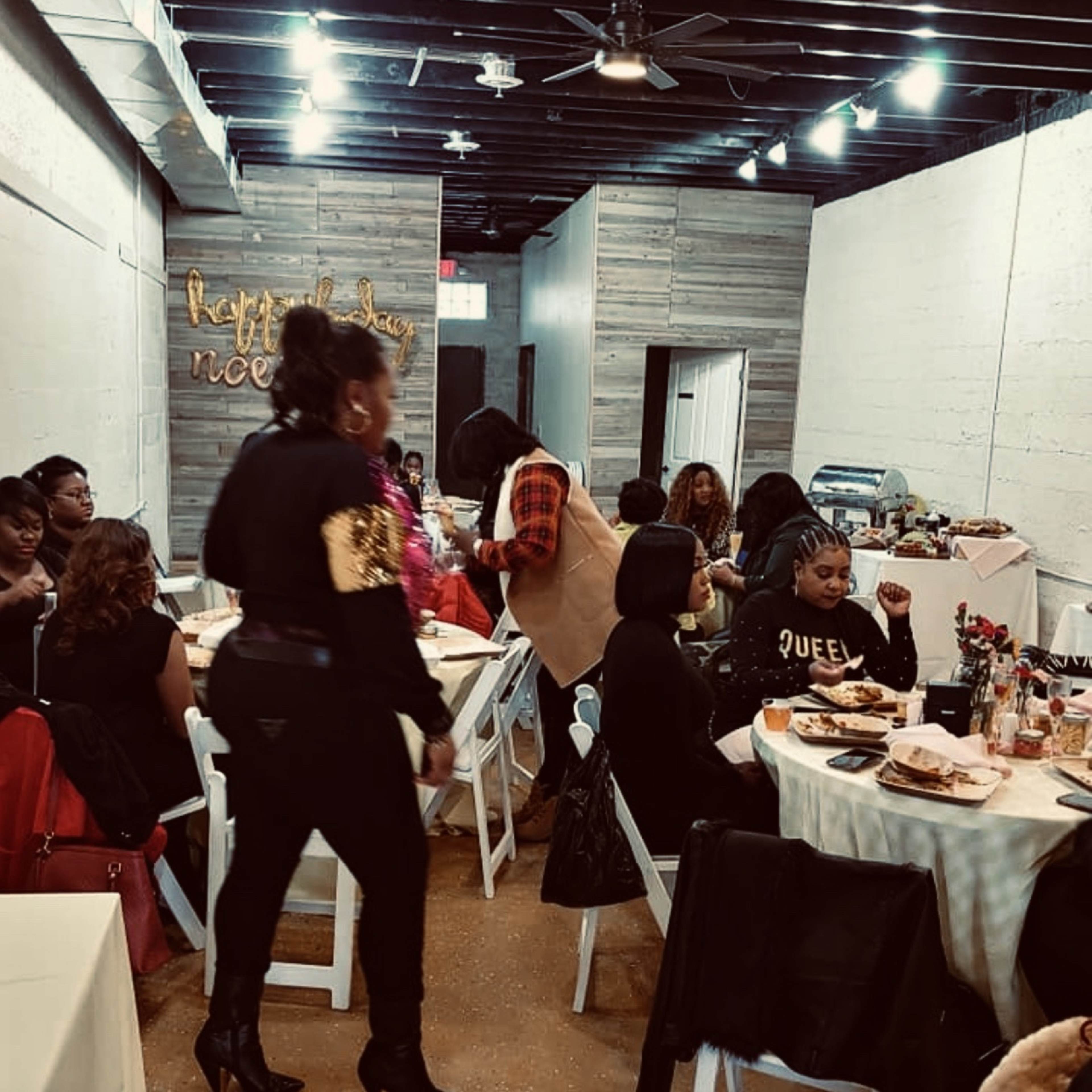 A spacious interior room arranged with rows of white chairs and black tables, with black-and-white photographs hanging on the walls.