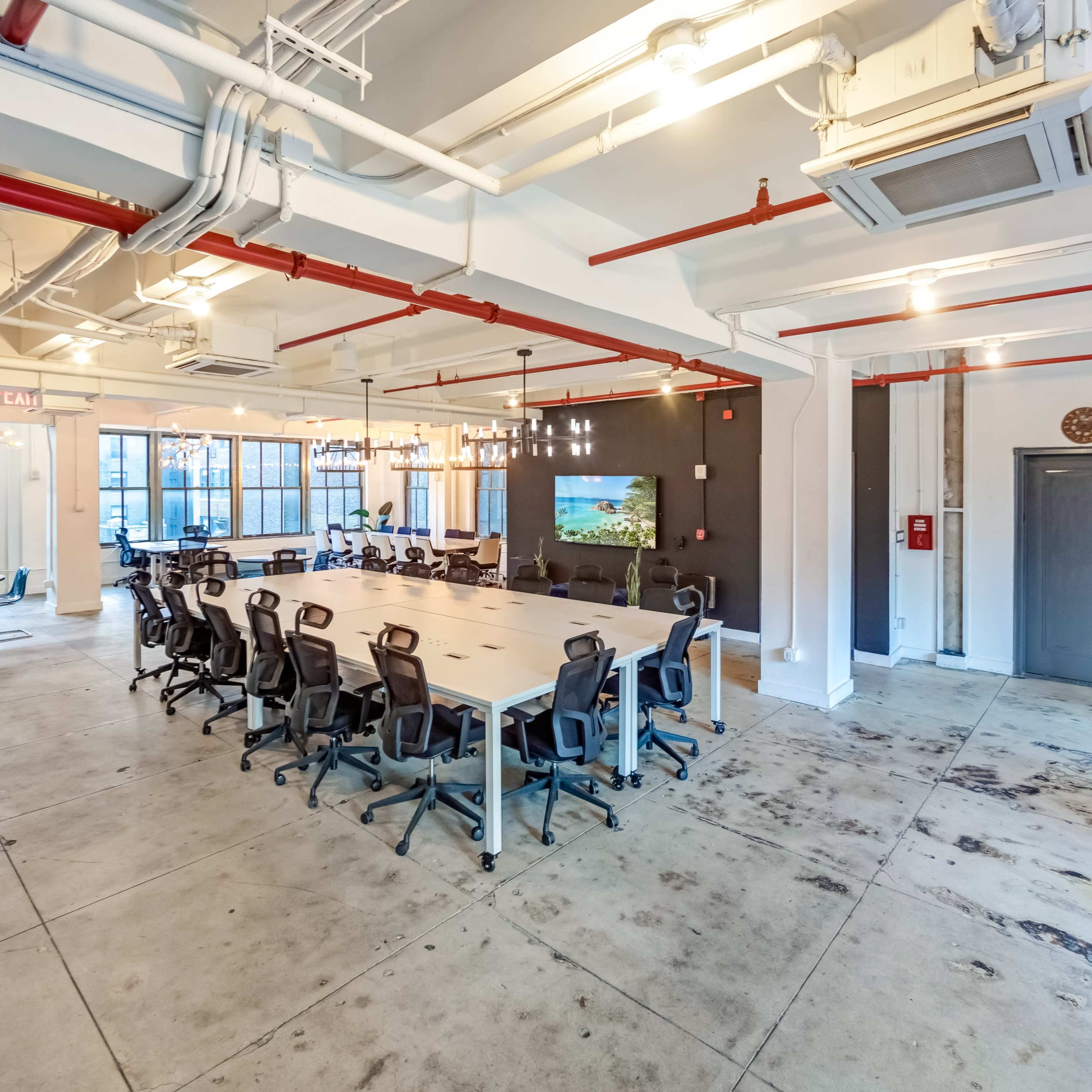 A spacious office area features a long conference table with ergonomic chairs, surrounded by large windows and modern decor.