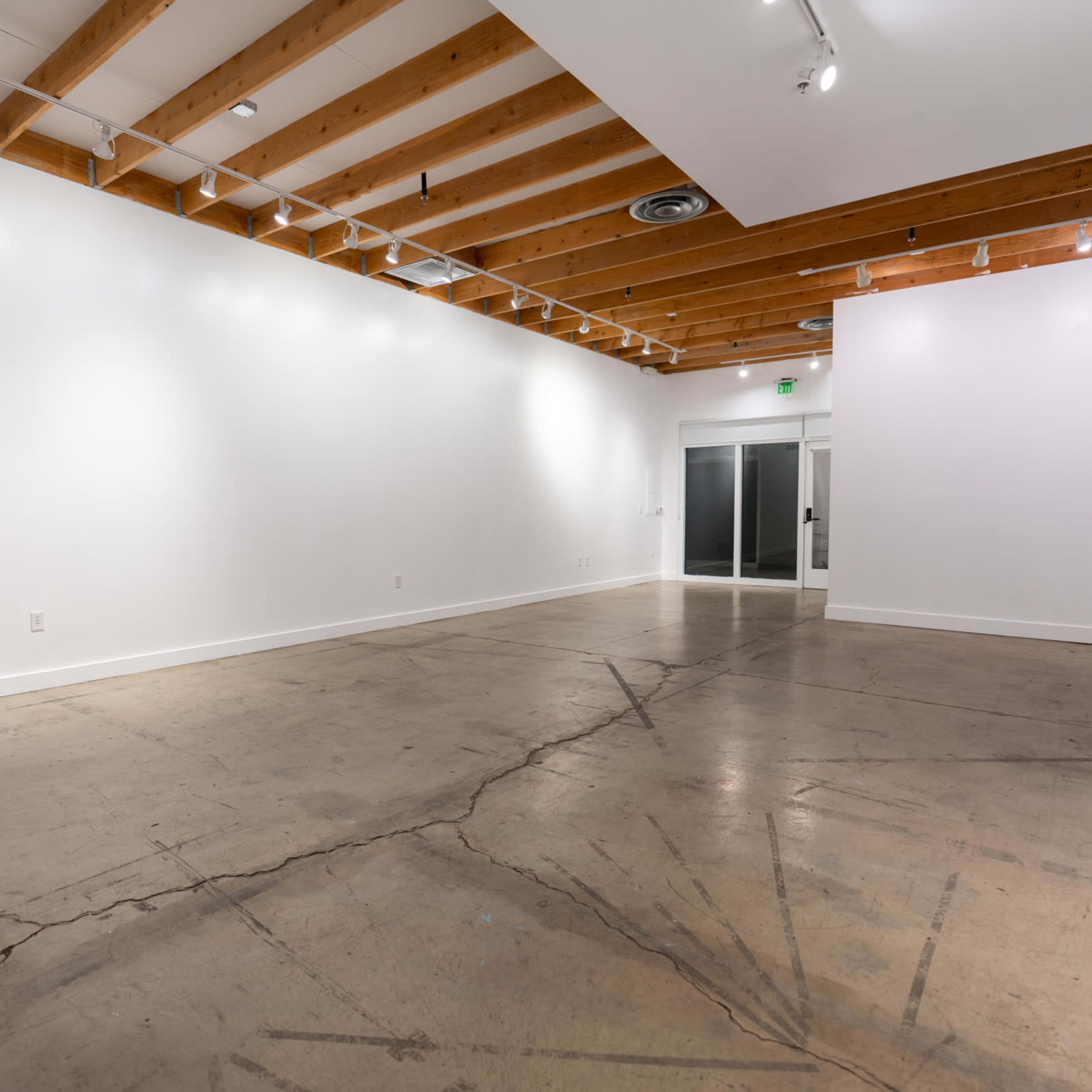 A spacious, empty room with concrete flooring and exposed wooden beams on the ceiling.