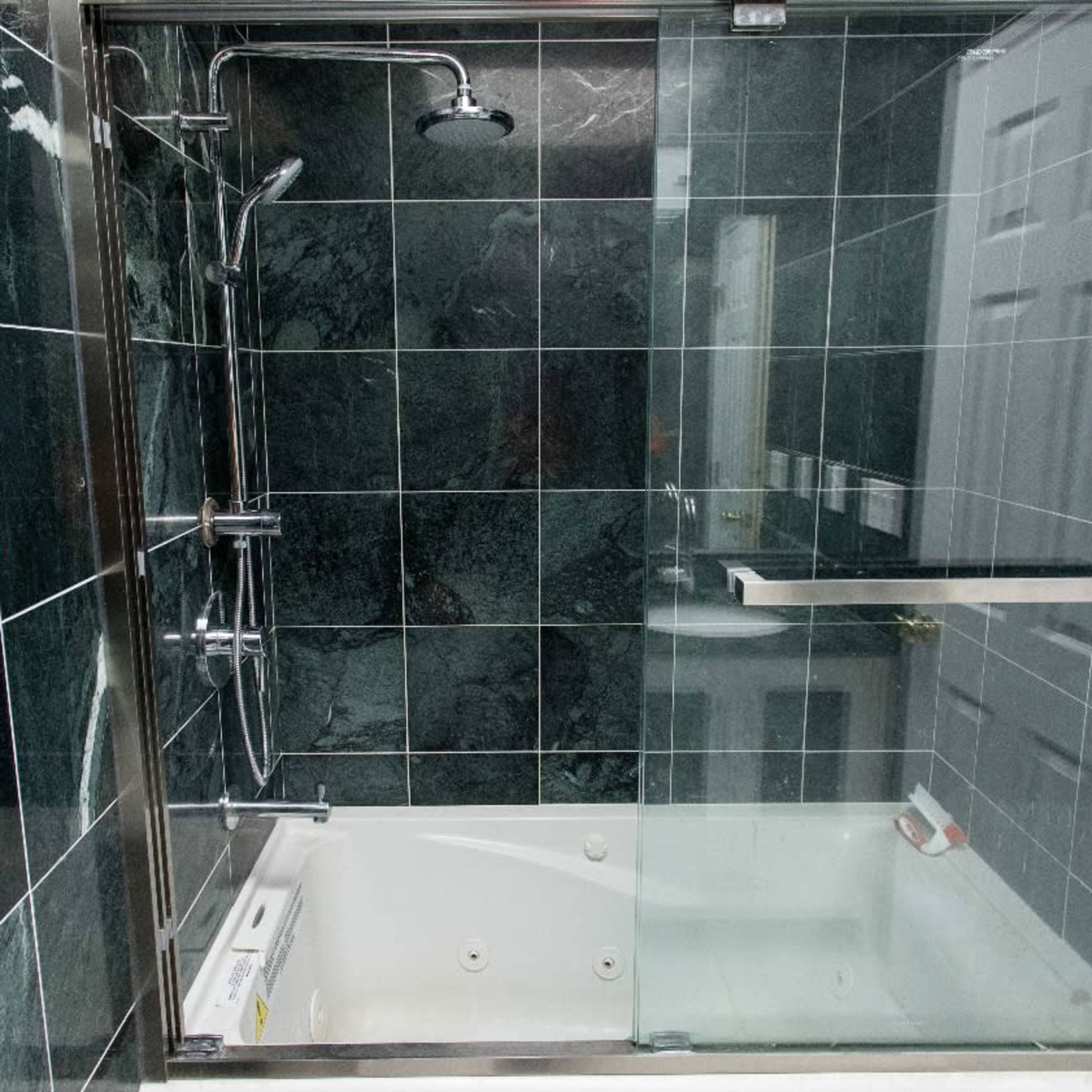 A bathroom featuring a glass-enclosed shower and a bathtub with marble-like green tiles on the walls.