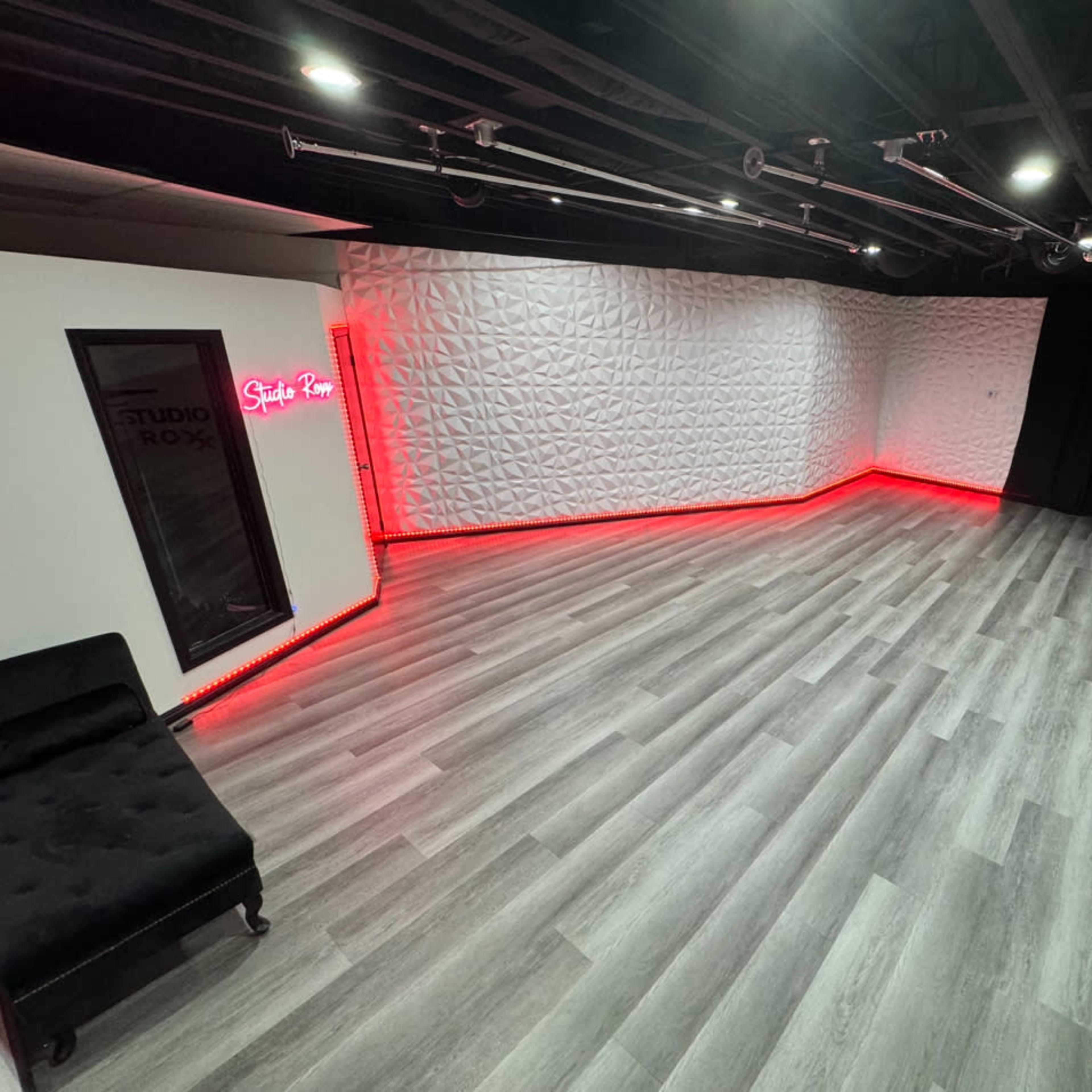 A spacious studio with gray wooden flooring and a white textured wall illuminated by red LED lights.