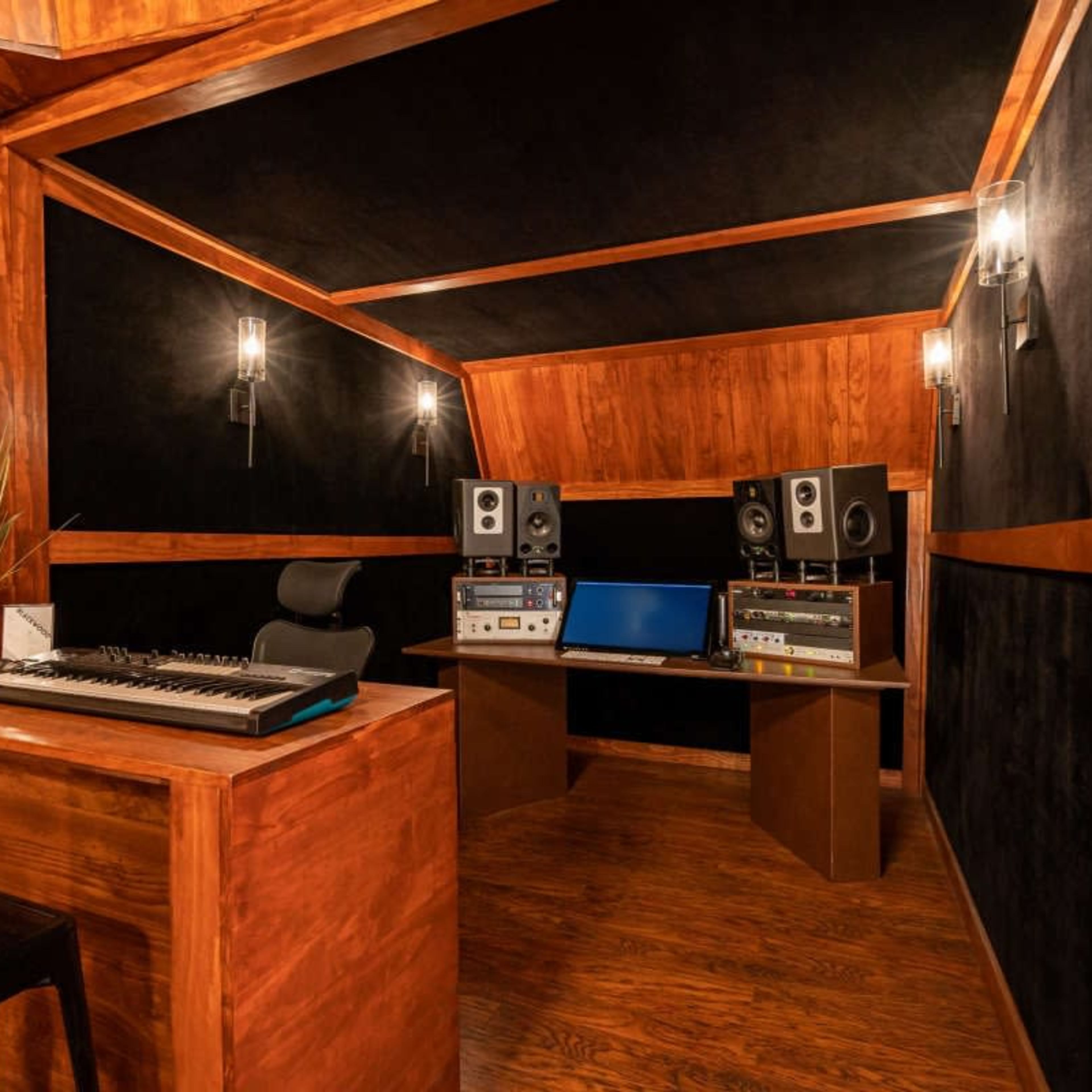 A wood-paneled recording studio with a desk, audio equipment, and soundproofing features.