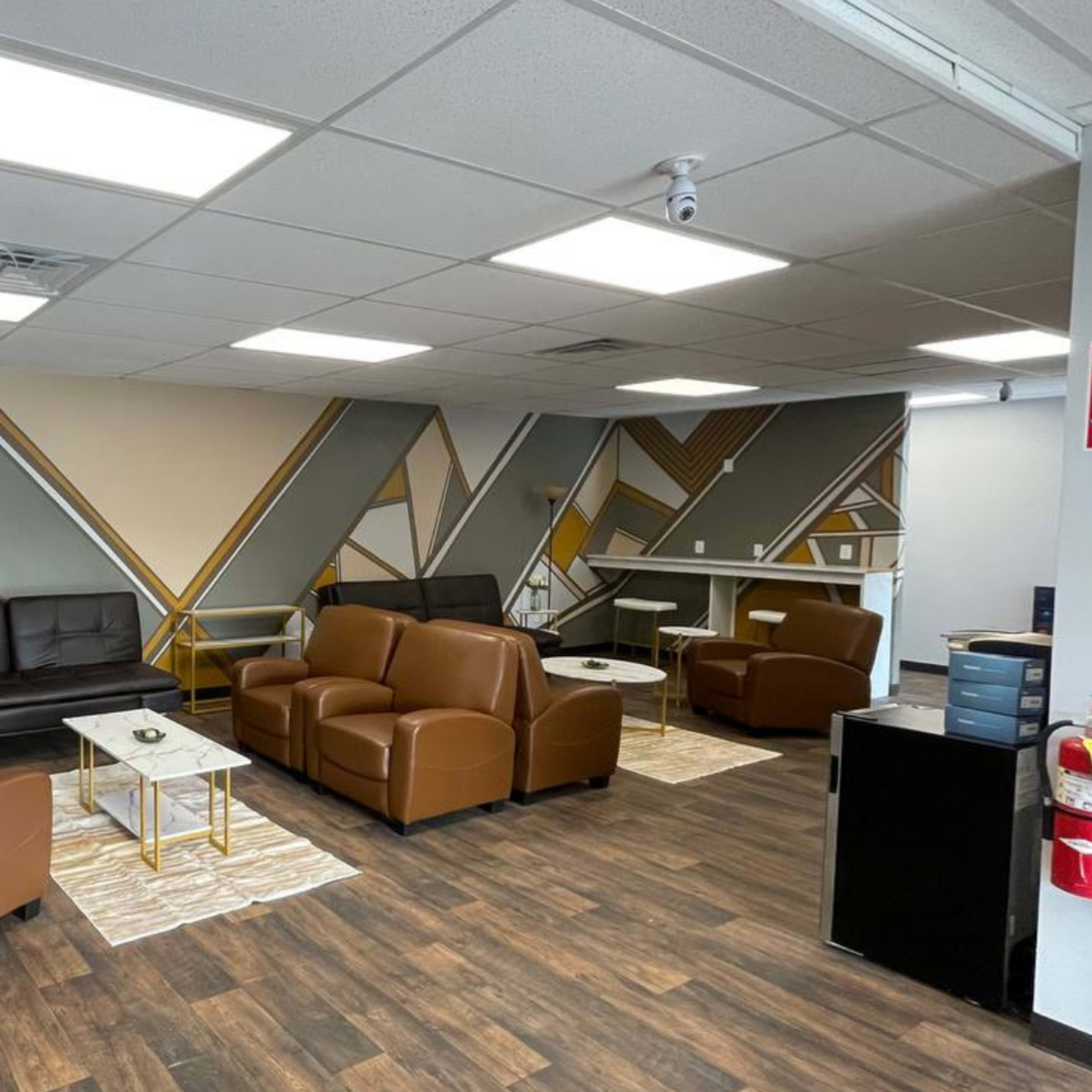 A modern lounge area featuring brown leather sofas, white side tables, and a geometric wall design in muted colors.
