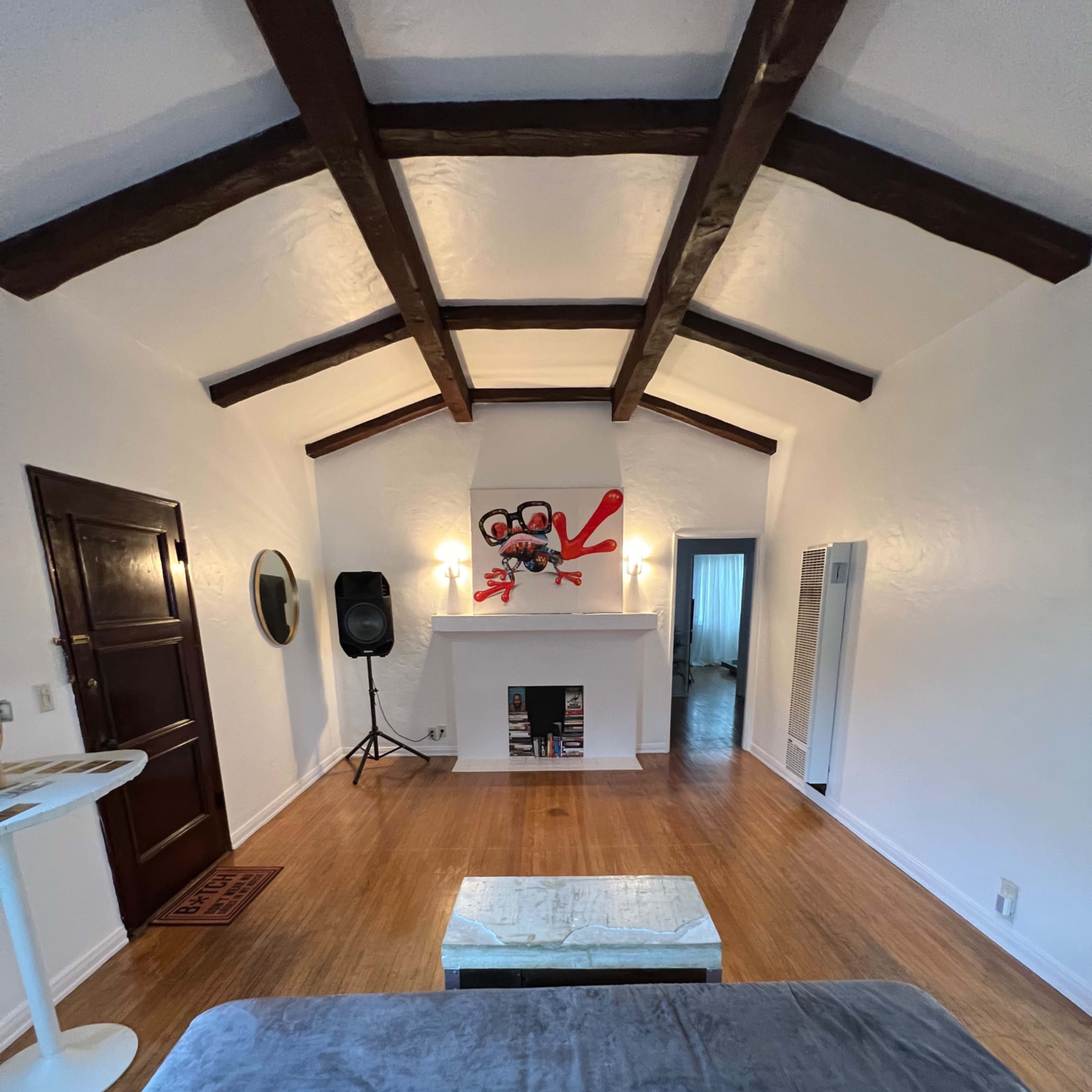 A spacious living room with wooden beam ceilings, a white fireplace, and a gray sofa facing a coffee table.