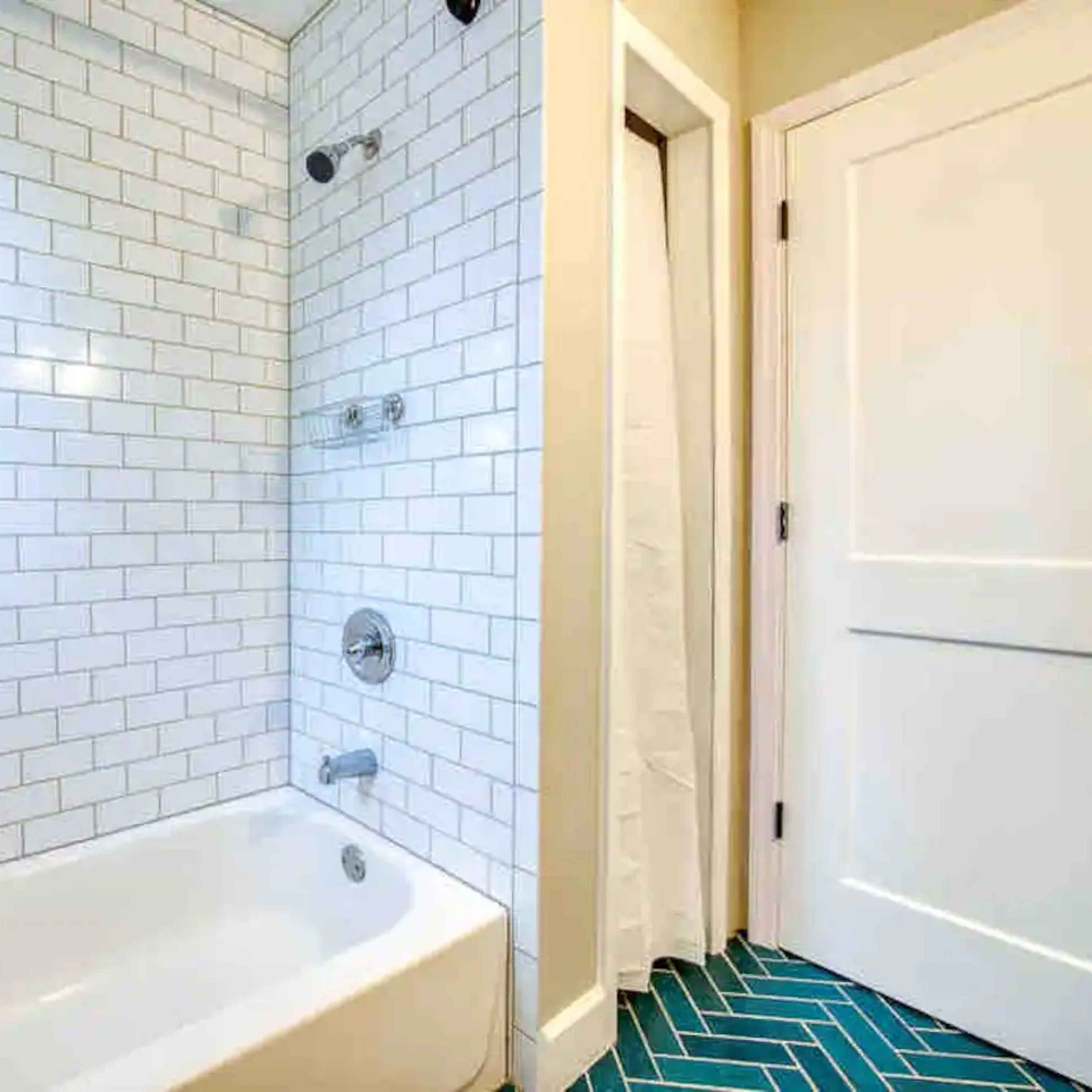 A bathroom with a white tiled shower area, a bathtub, and a blue patterned floor.