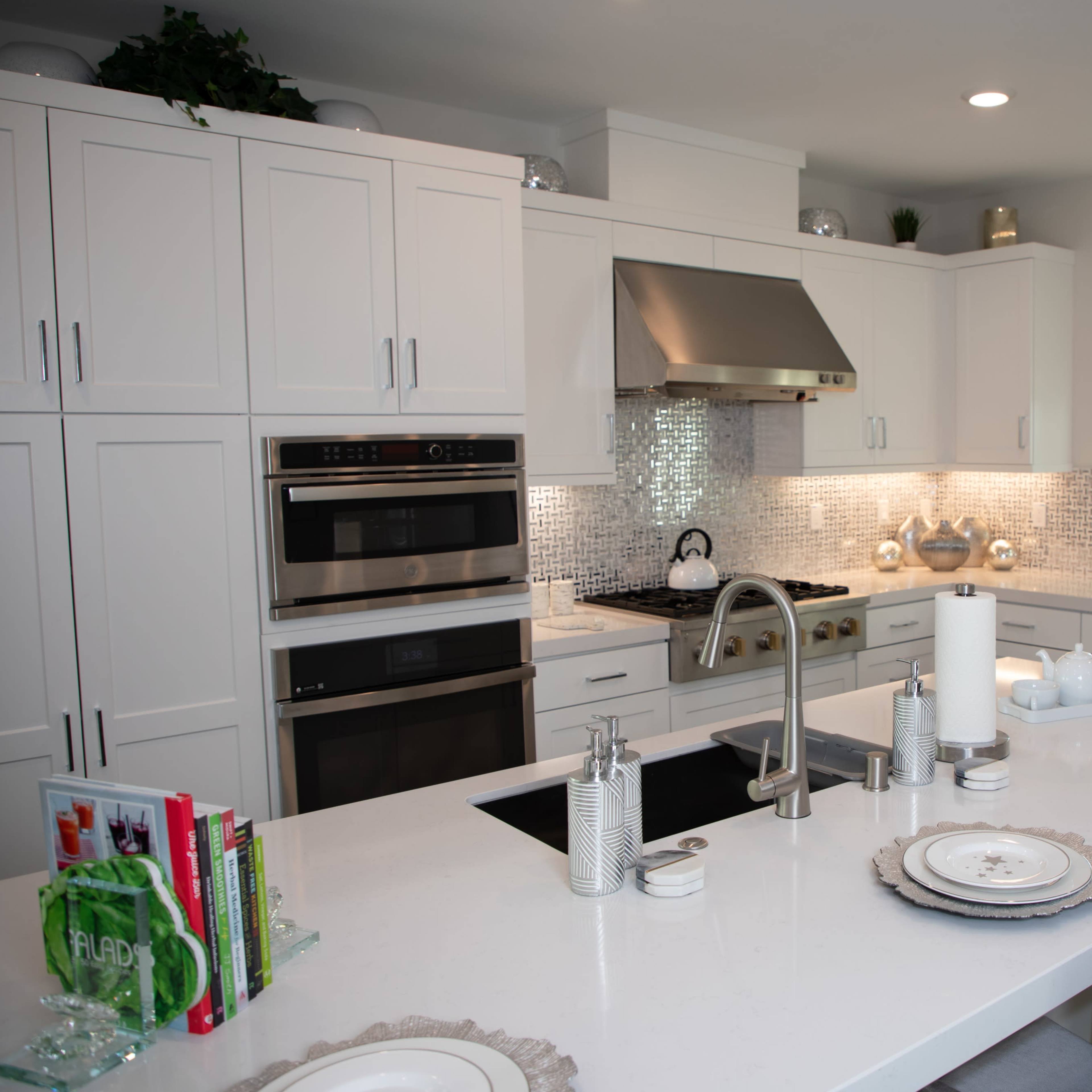 A modern kitchen with white cabinetry, stainless steel appliances, a large island with seating, and a tiled backsplash.