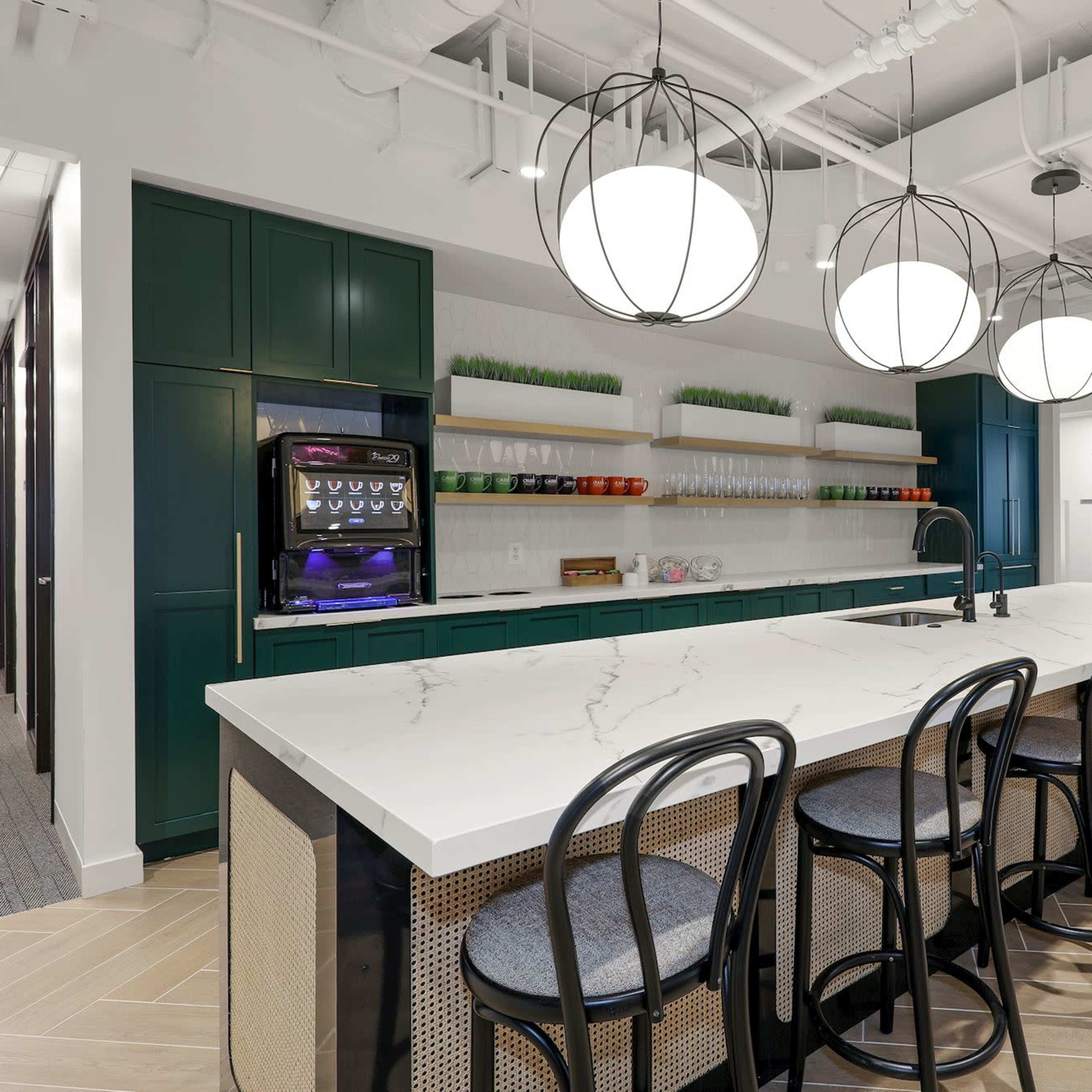 A modern kitchen area with a large white marble island and sleek black chairs, illuminated by round pendant lights.