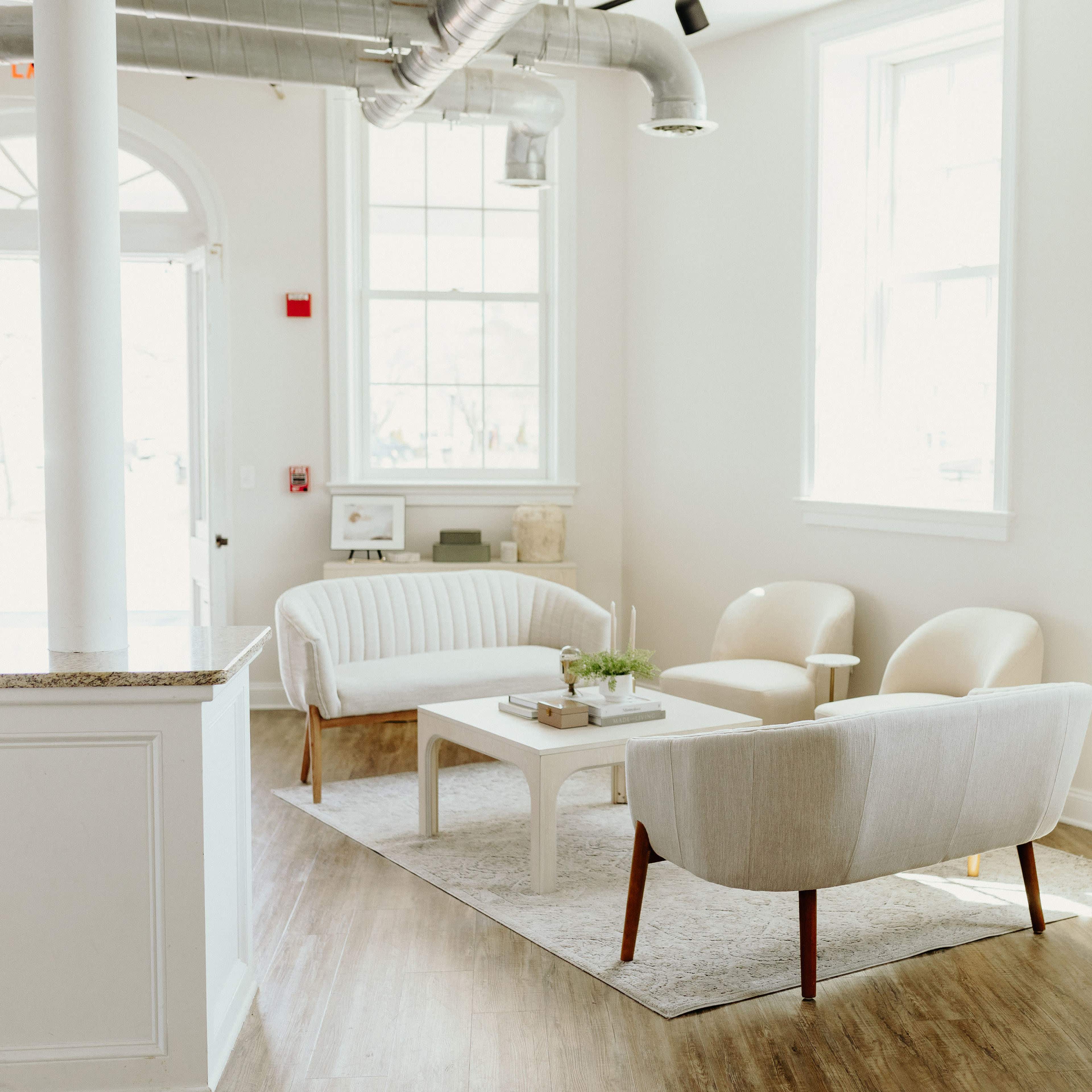 A bright, minimalistic interior space featuring a light-colored seating area with two armchairs, a sofa, and a coffee table on a plush rug.