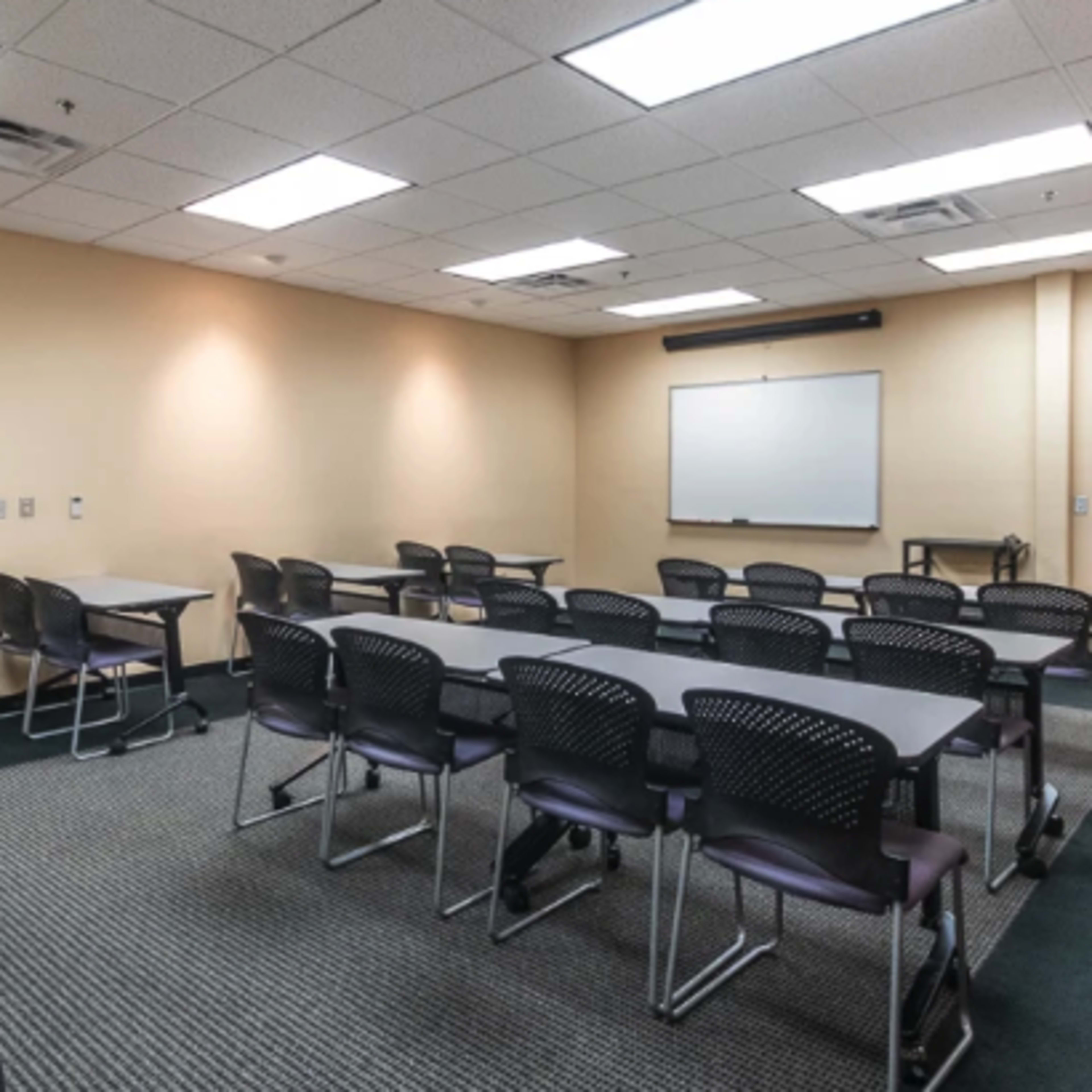 A meeting room arranged with several tables and chairs, featuring a whiteboard and a door leading to another space.