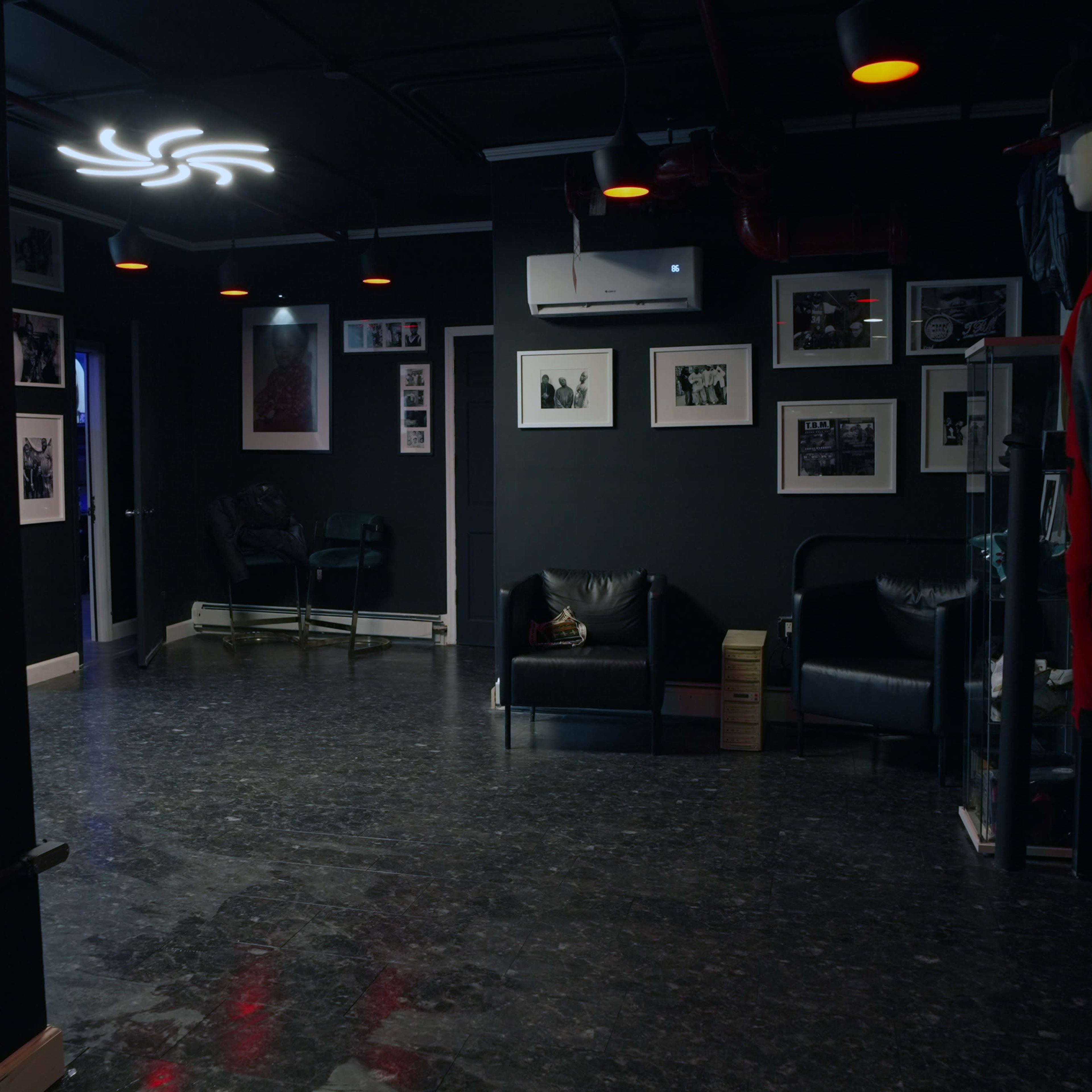 The room features black walls, two leather sofas, and several framed black-and-white photographs hanging on the walls.