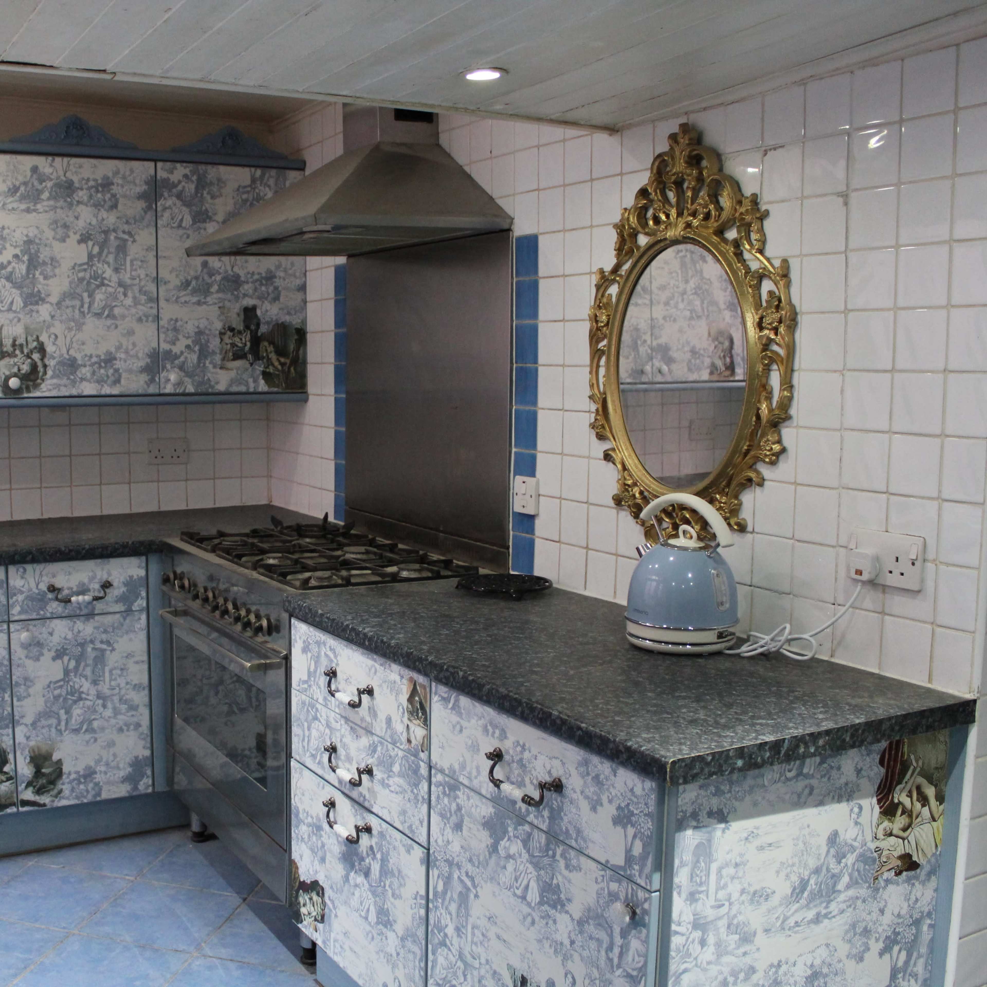 A kitchen with blue and white patterned cabinets, a stainless steel range hood, and a decorative mirror on the wall.