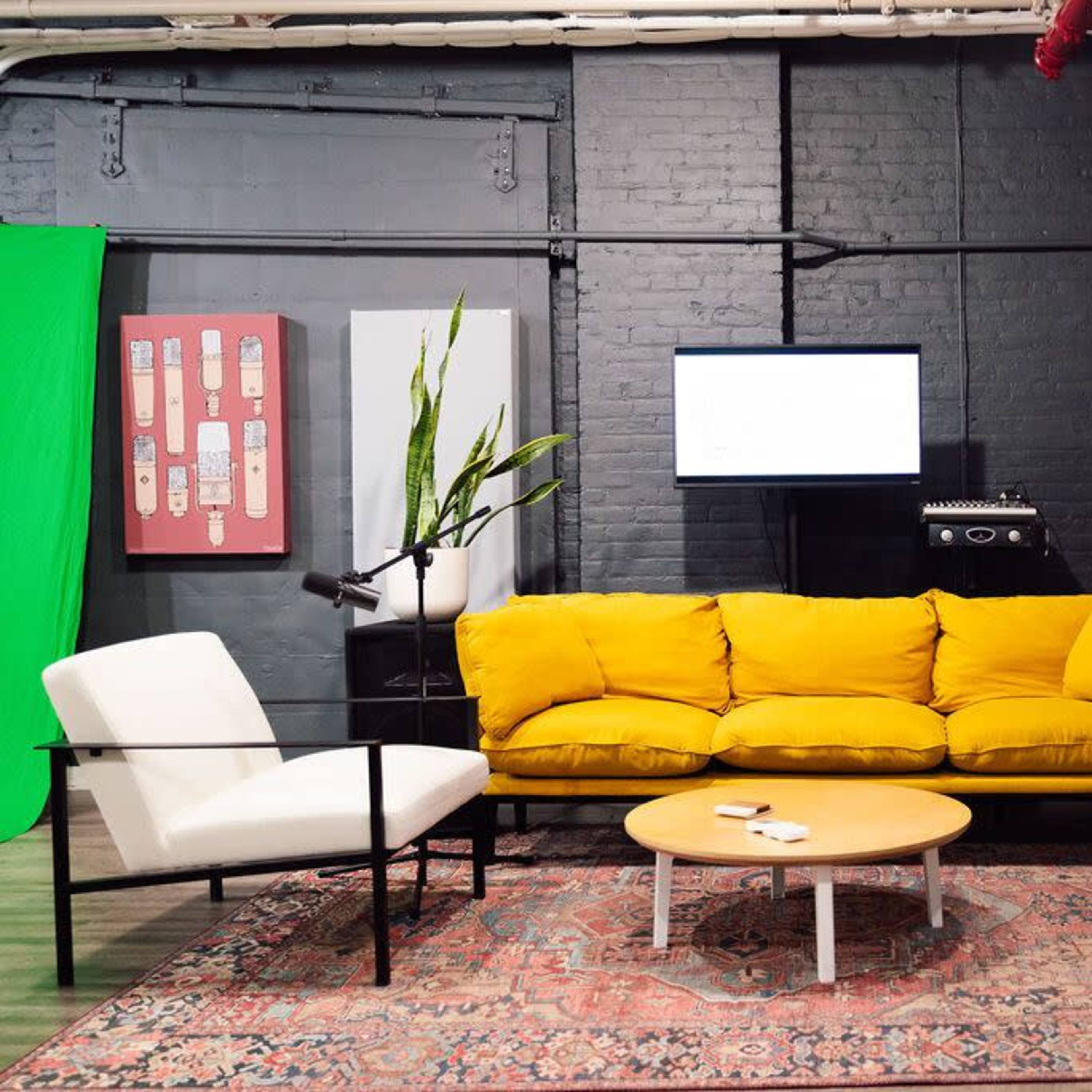 A modern living room featuring a bright yellow couch, two white armchairs, a round coffee table, and decorative plants, set against a backdrop of black brick walls and red curtains.