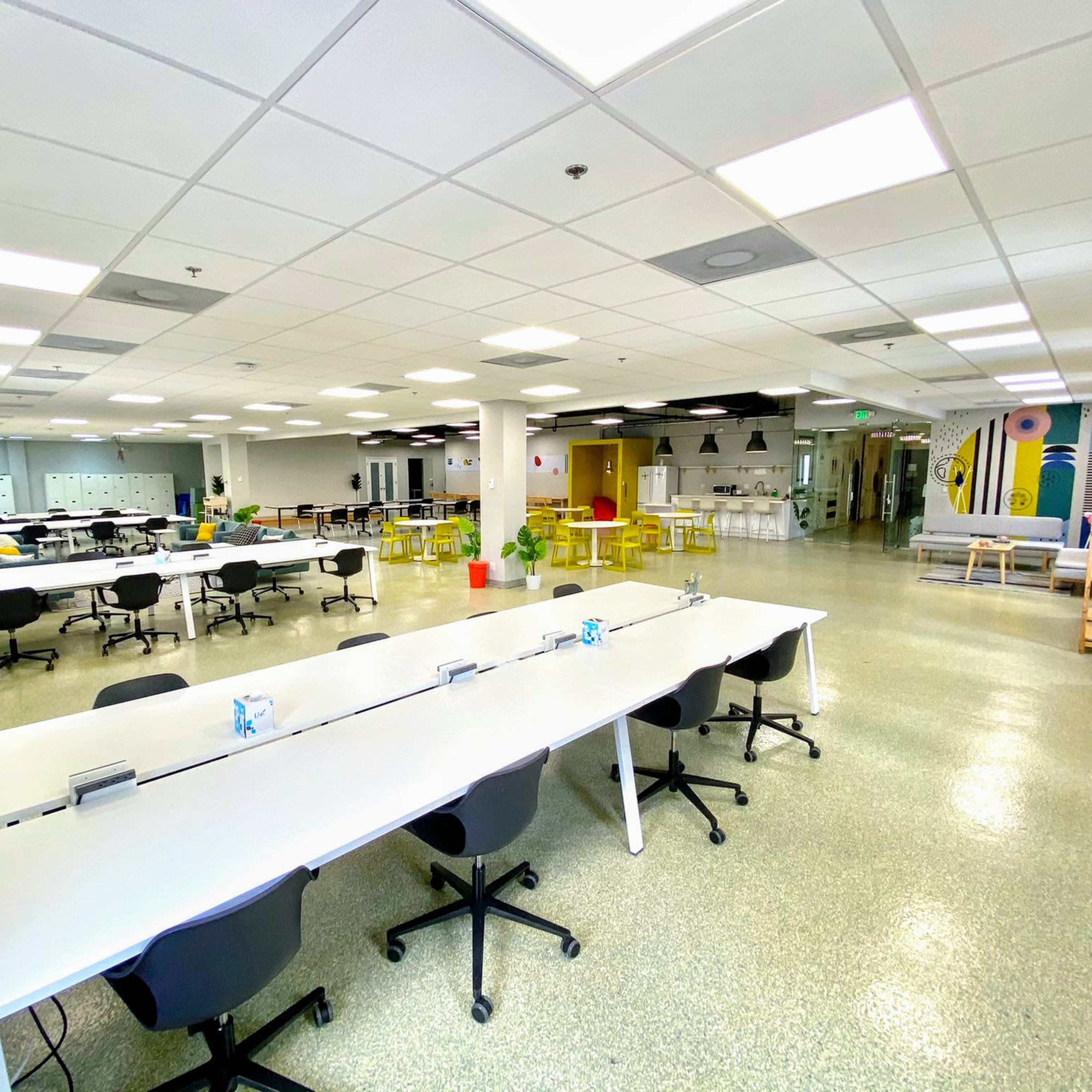A spacious, brightly lit classroom with several long tables and black chairs arranged in a layout conducive to collaboration.