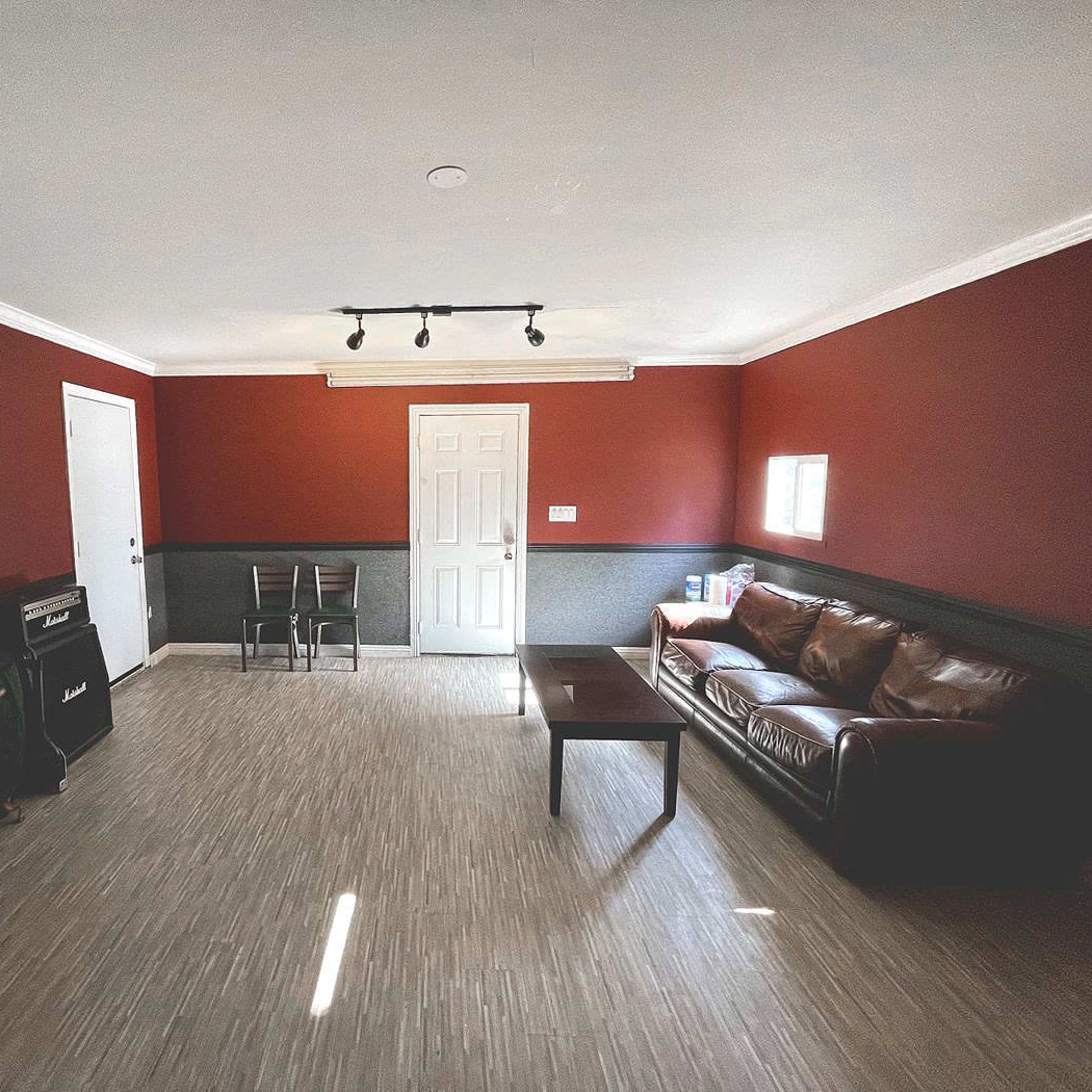 The room features a brown leather sofa, a coffee table, a door, and two chairs against a red and gray wall.