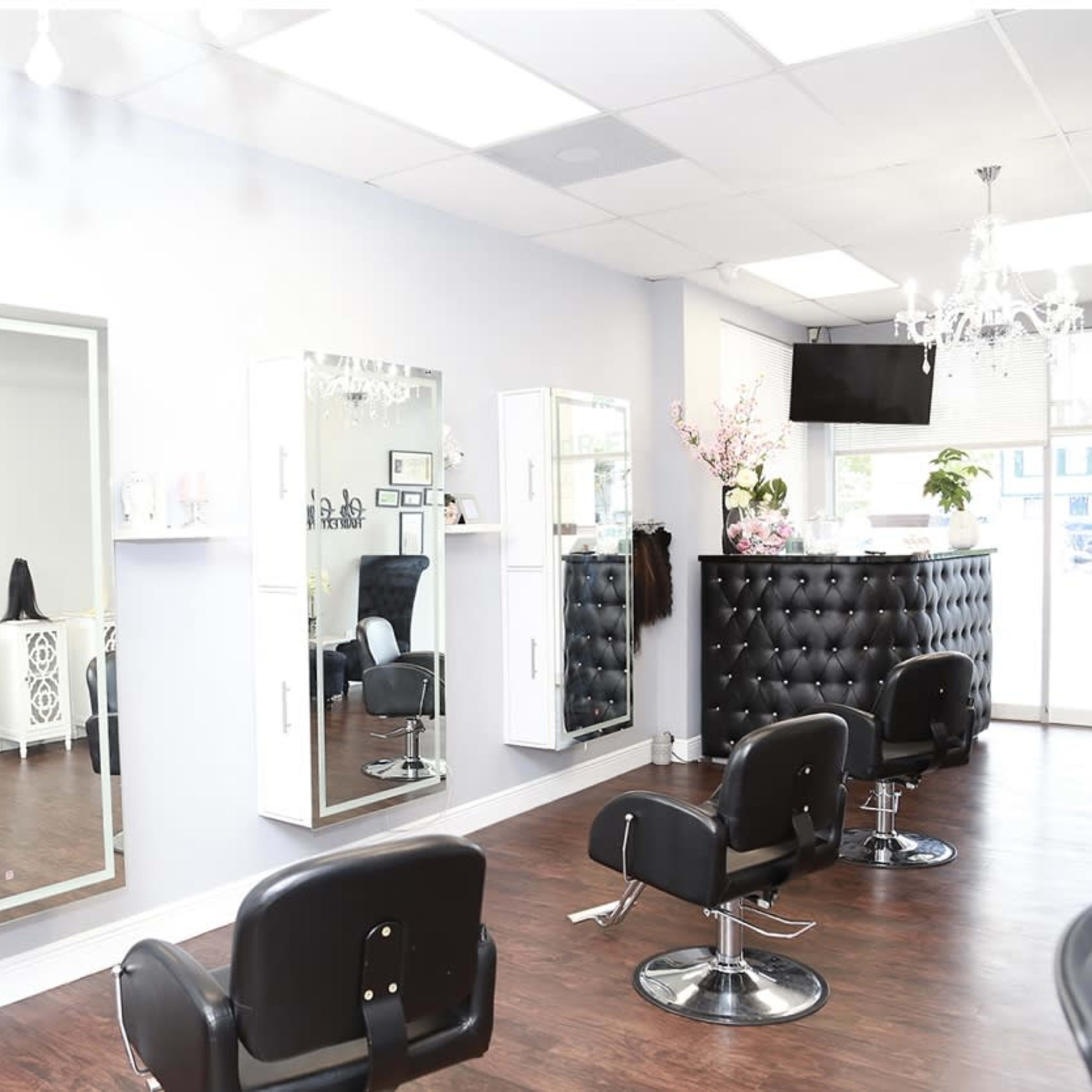 A modern hair salon interior featuring black styling chairs, large mirrors, and a decorative reception area.
