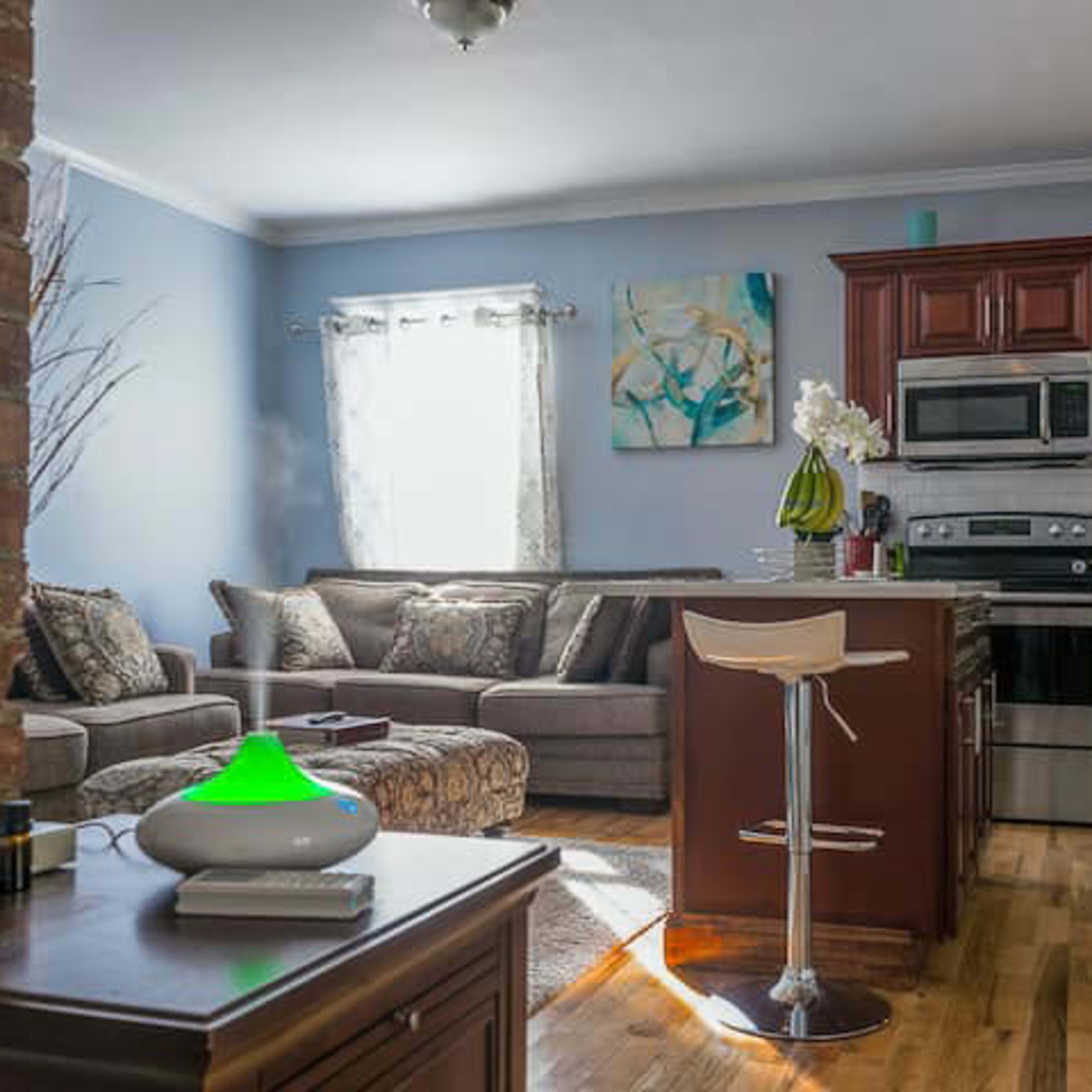 A modern living area and kitchen combination featuring a comfortable sofa, a kitchen island with bar stools, and wooden flooring.