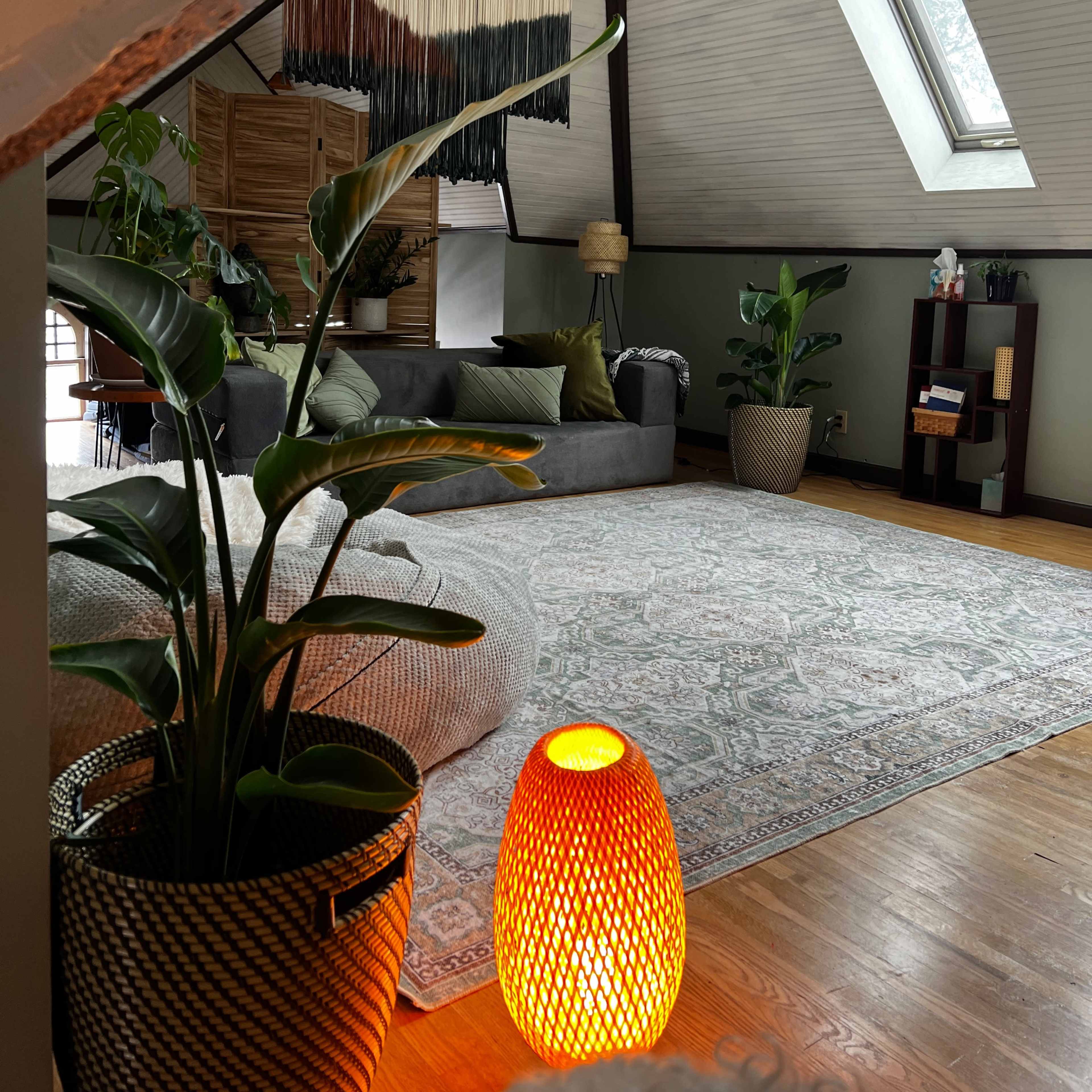 A cozy attic living room features a gray sofa, a textured area rug, potted plants, and a unique amber lamp.
