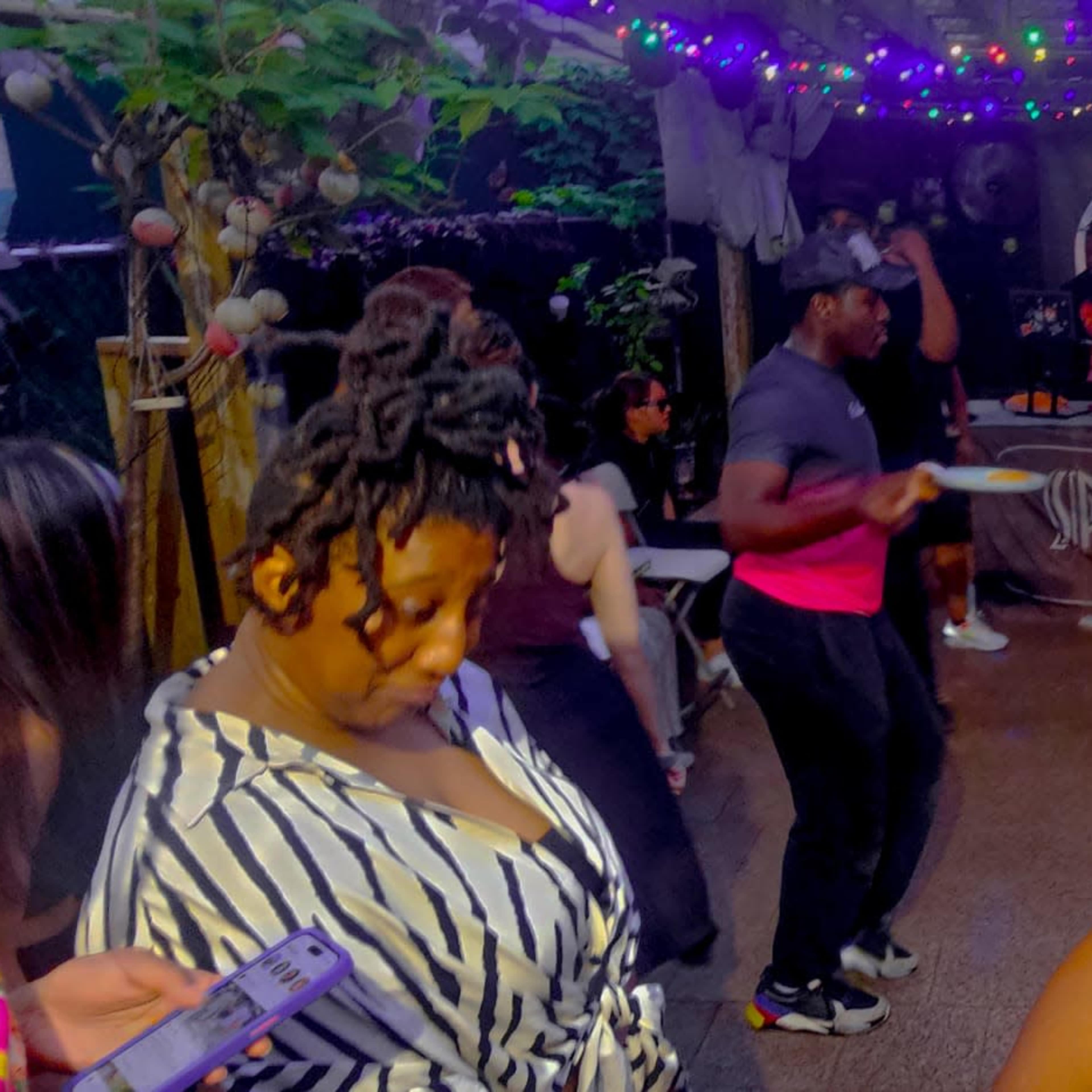 A group of people is dancing and socializing at an outdoor party decorated with colorful lights.