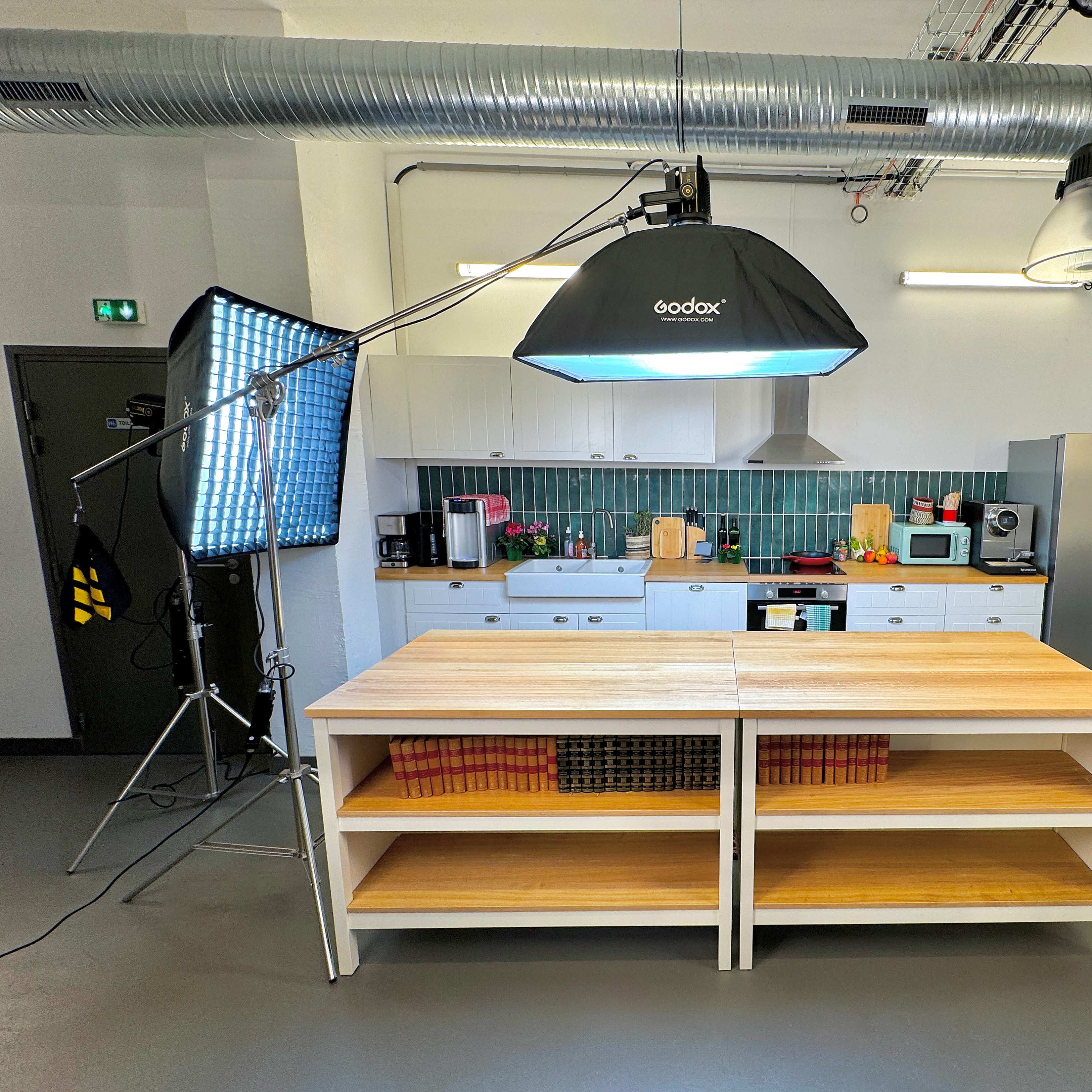 A spacious kitchen with modern appliances, featuring a central wooden preparation table and ample lighting set up for photography.