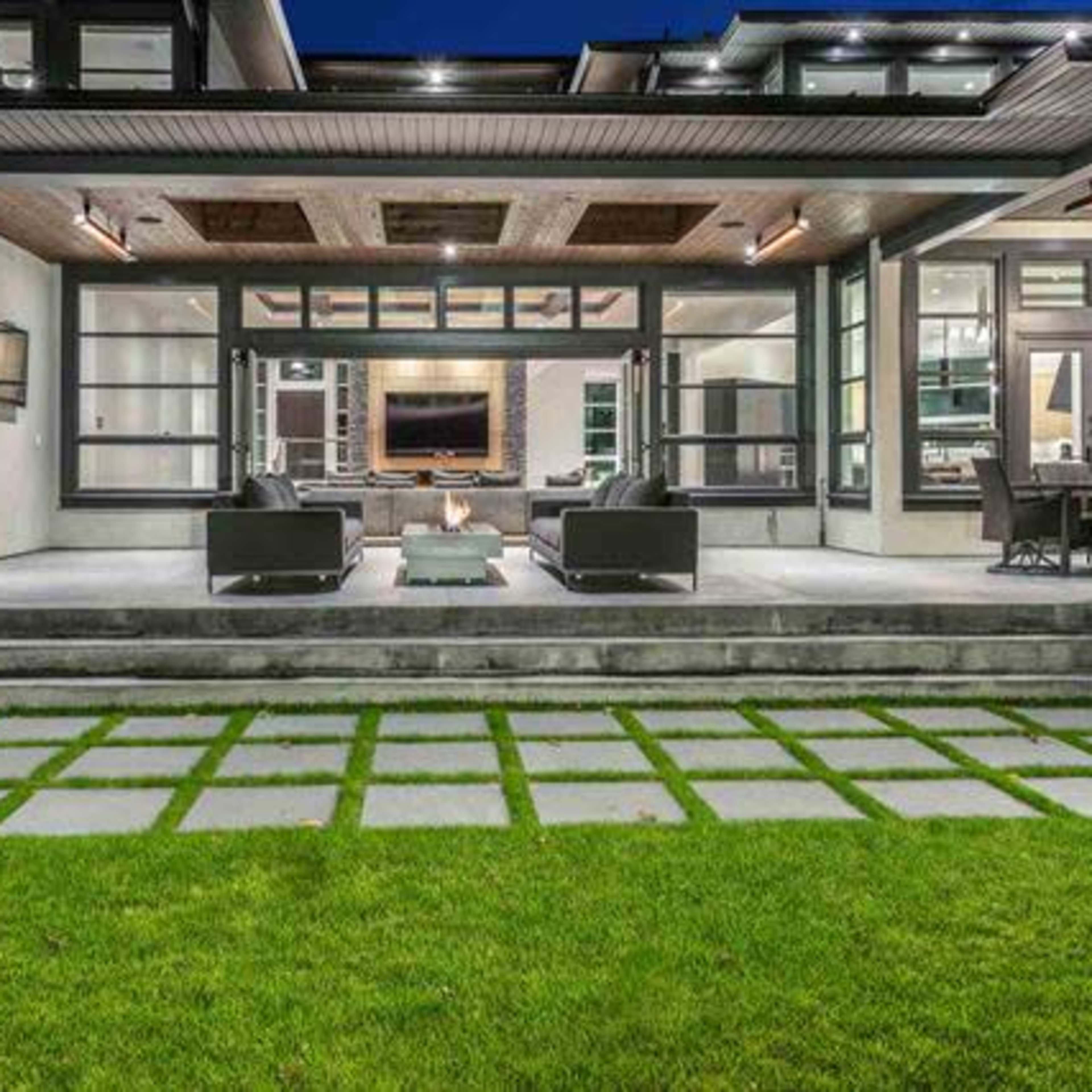 A modern home with a spacious outdoor patio, featuring seating areas and a neatly manicured lawn with stone pathways.