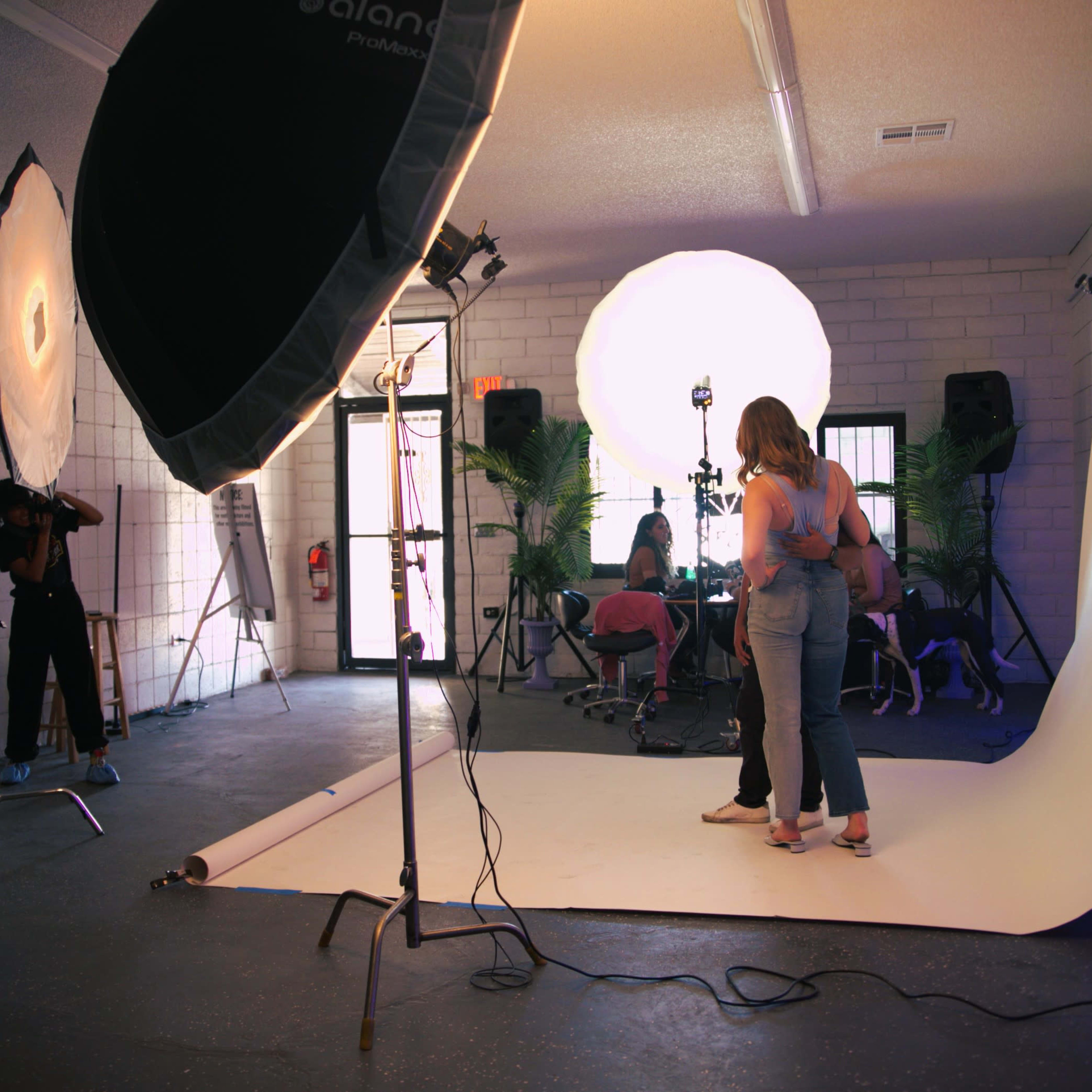 A photography studio is set up with multiple lights, a backdrop, and several people engaged in a photoshoot.