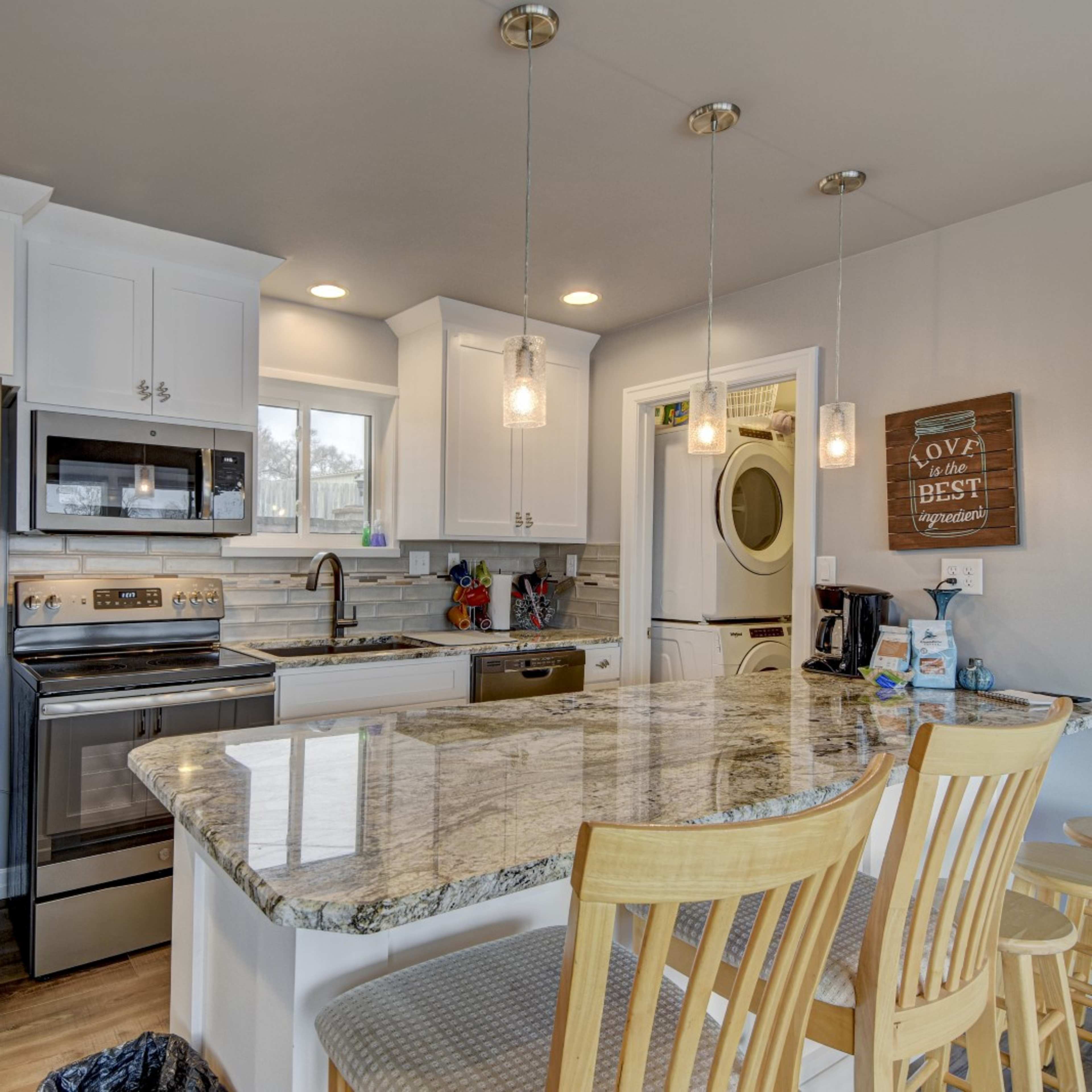 A modern kitchen with white cabinetry, stainless steel appliances, a granite countertop, and bar seating.