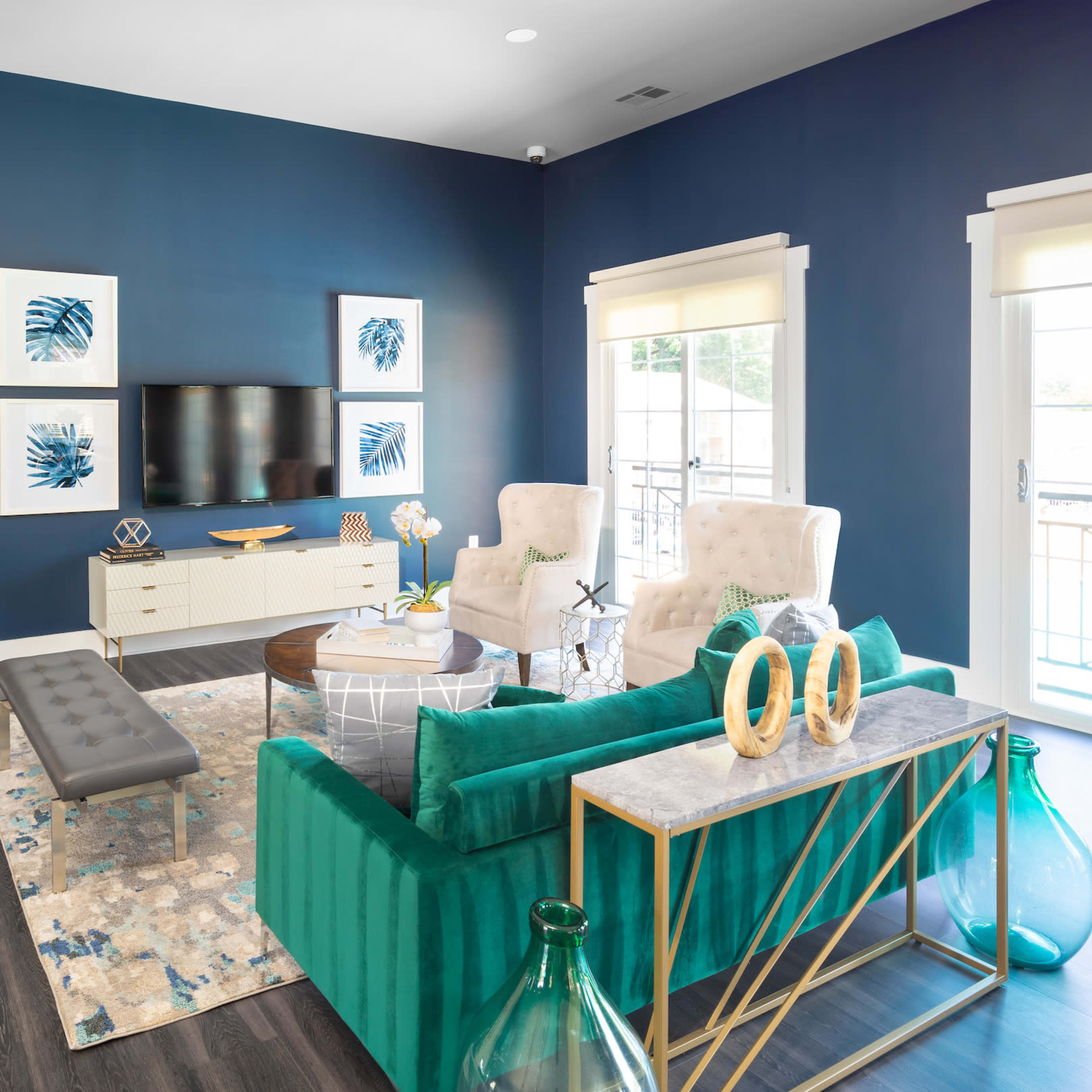 A modern living room features blue walls, a large television mounted on the wall, plush seating, and decorative accessories on a coffee table.