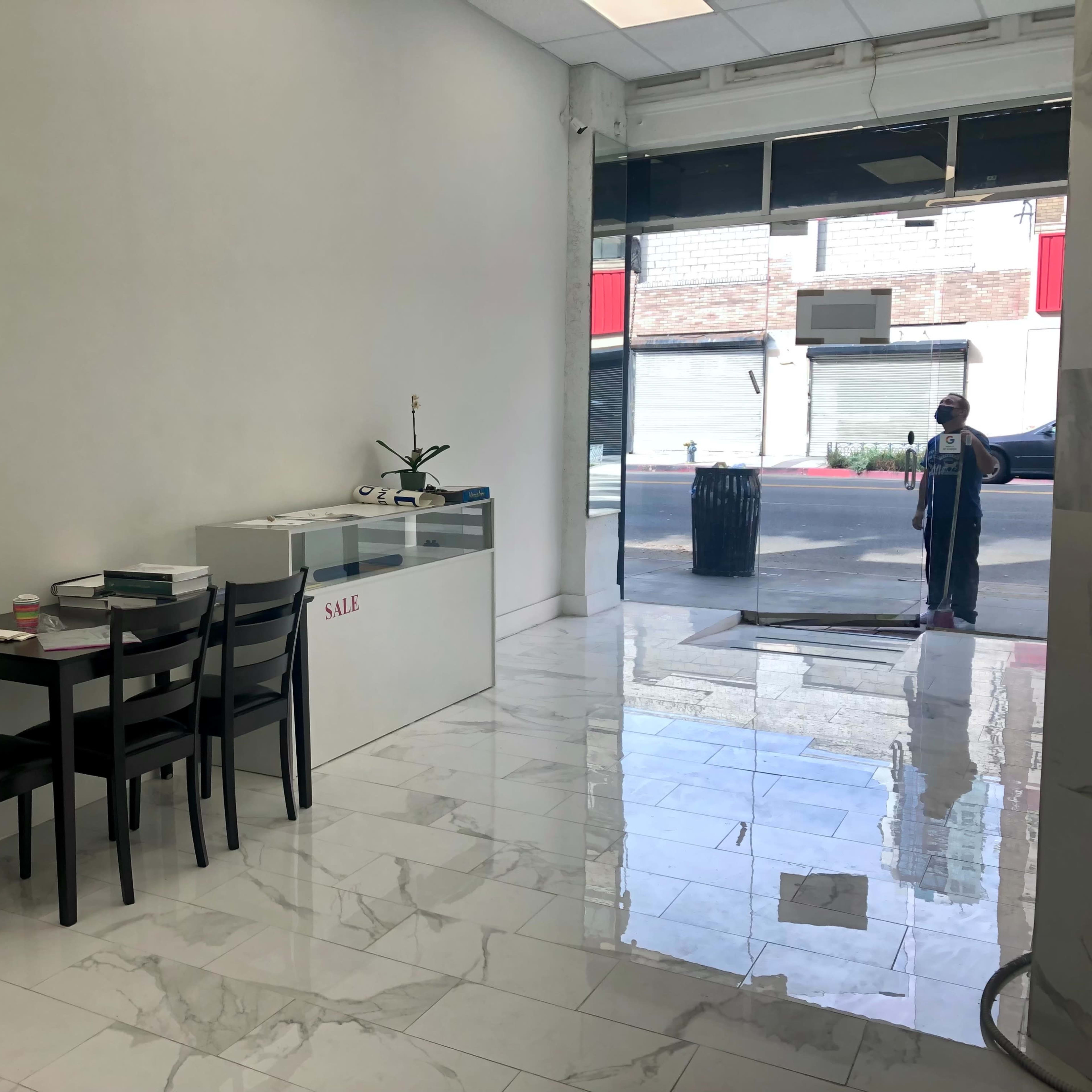 A clean, empty retail space features a display counter and a few black chairs near the entrance, with a person standing outside.