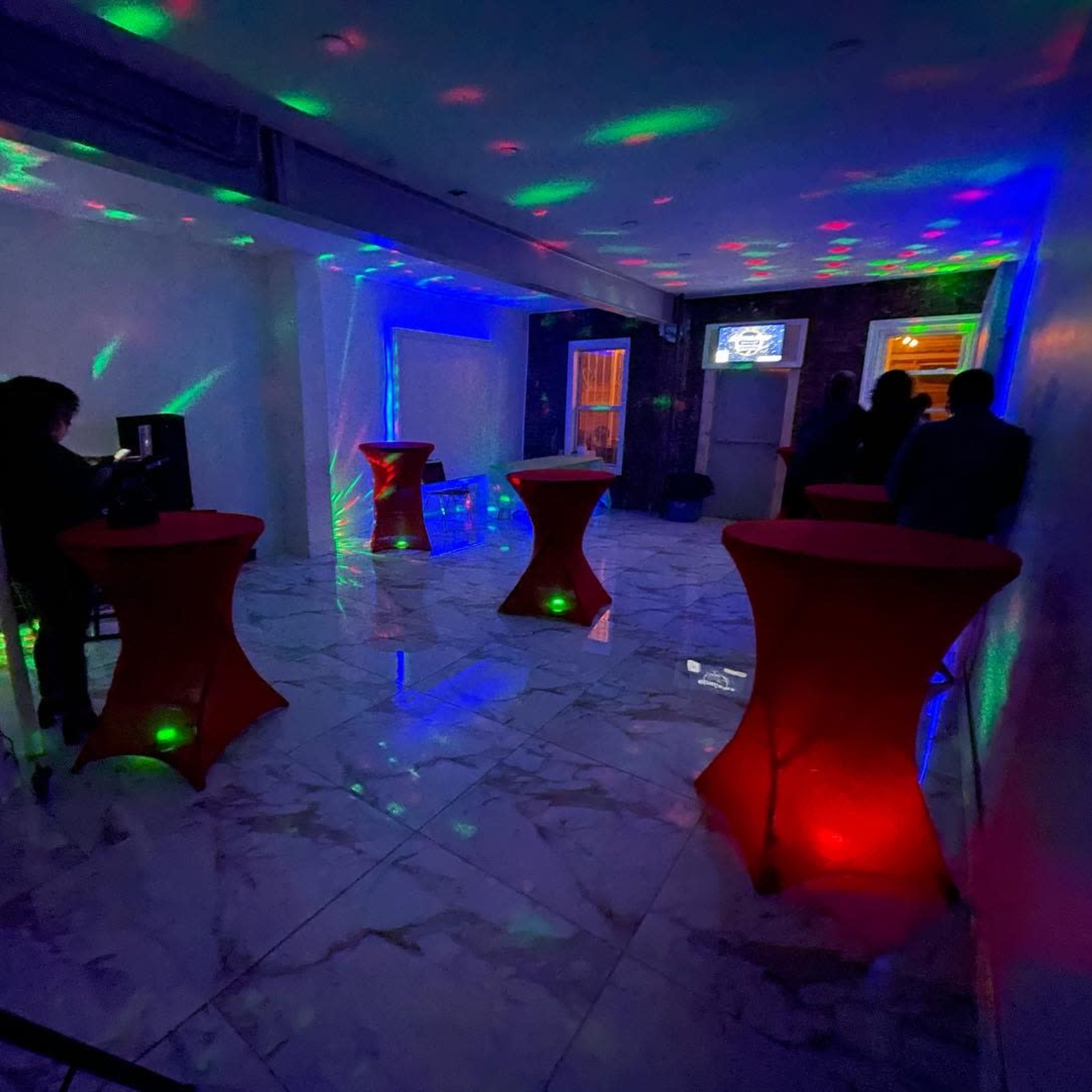 The scene shows a dimly lit room with four red cocktail tables surrounded by colorful light patterns projected on the marble floor.