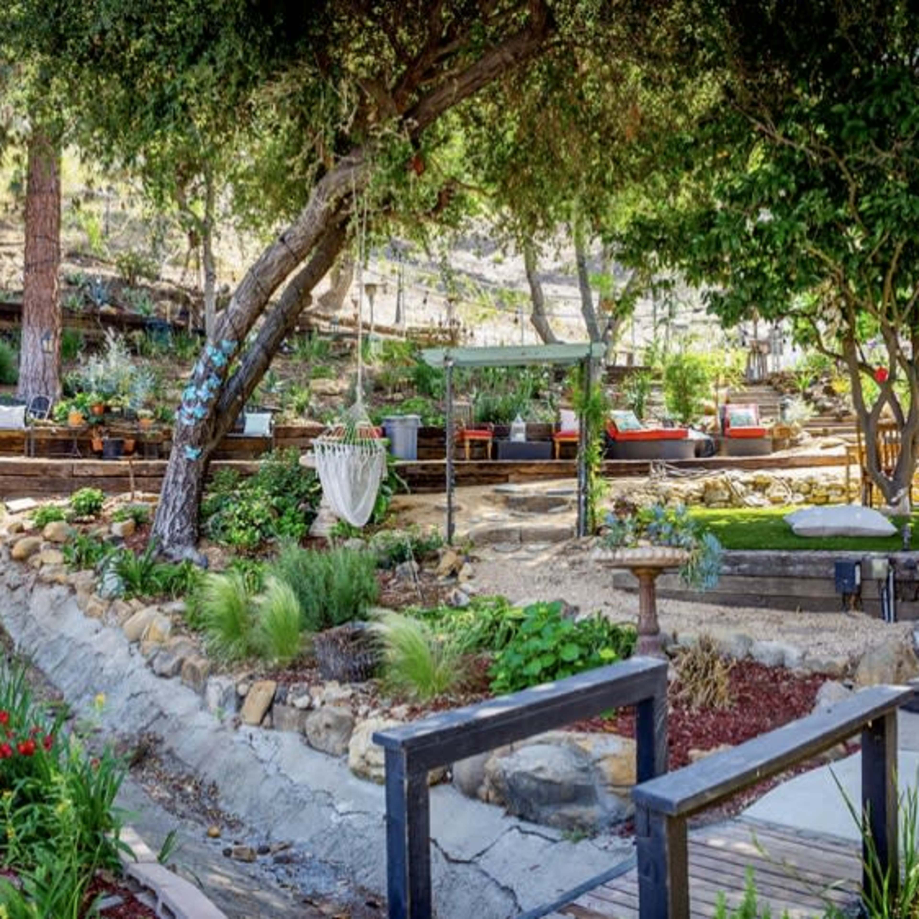 A landscaped garden with stone paths, terraced seating areas, and various plants and trees.