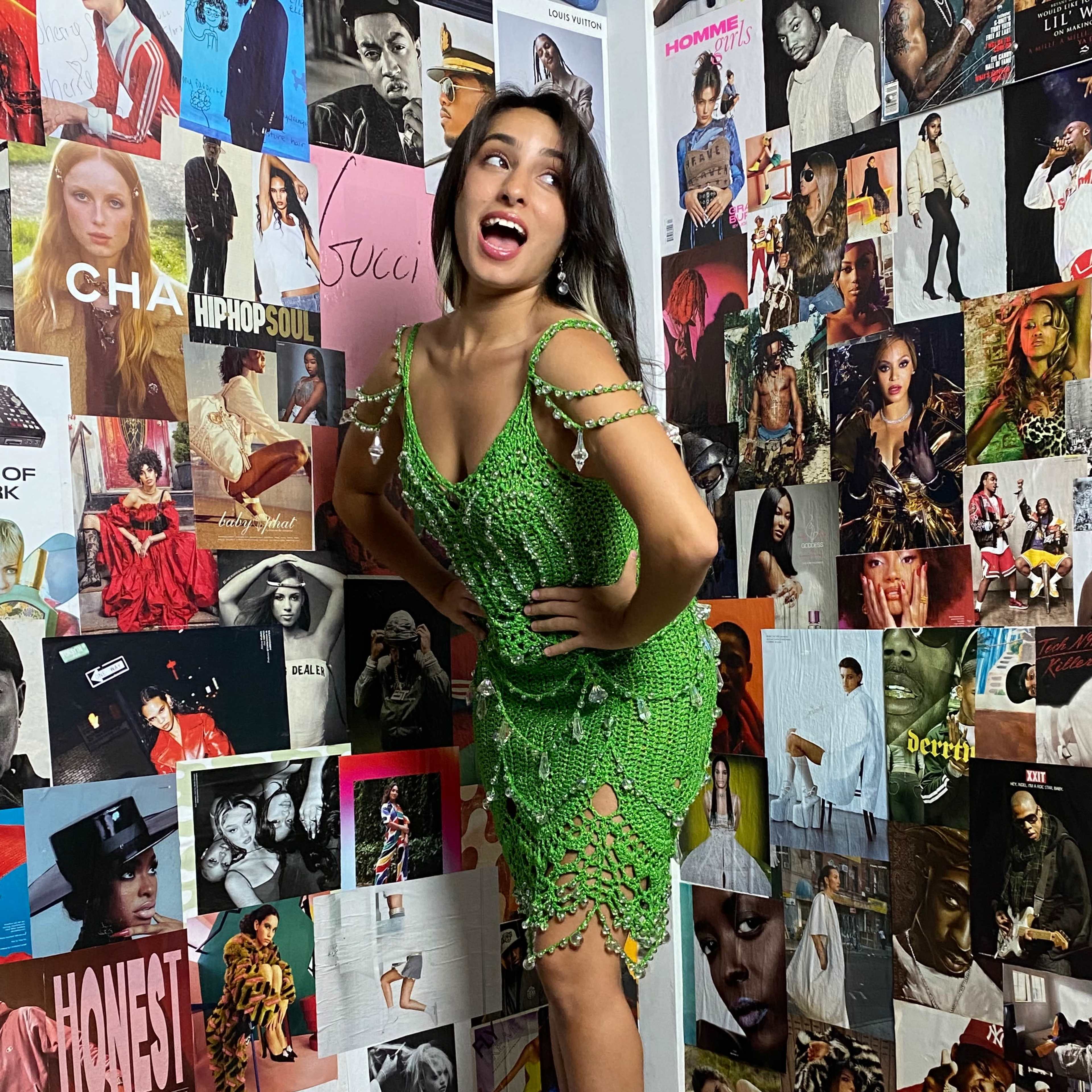 A woman poses playfully in a green crocheted dress against a vibrant collage of magazine covers and fashion posters.