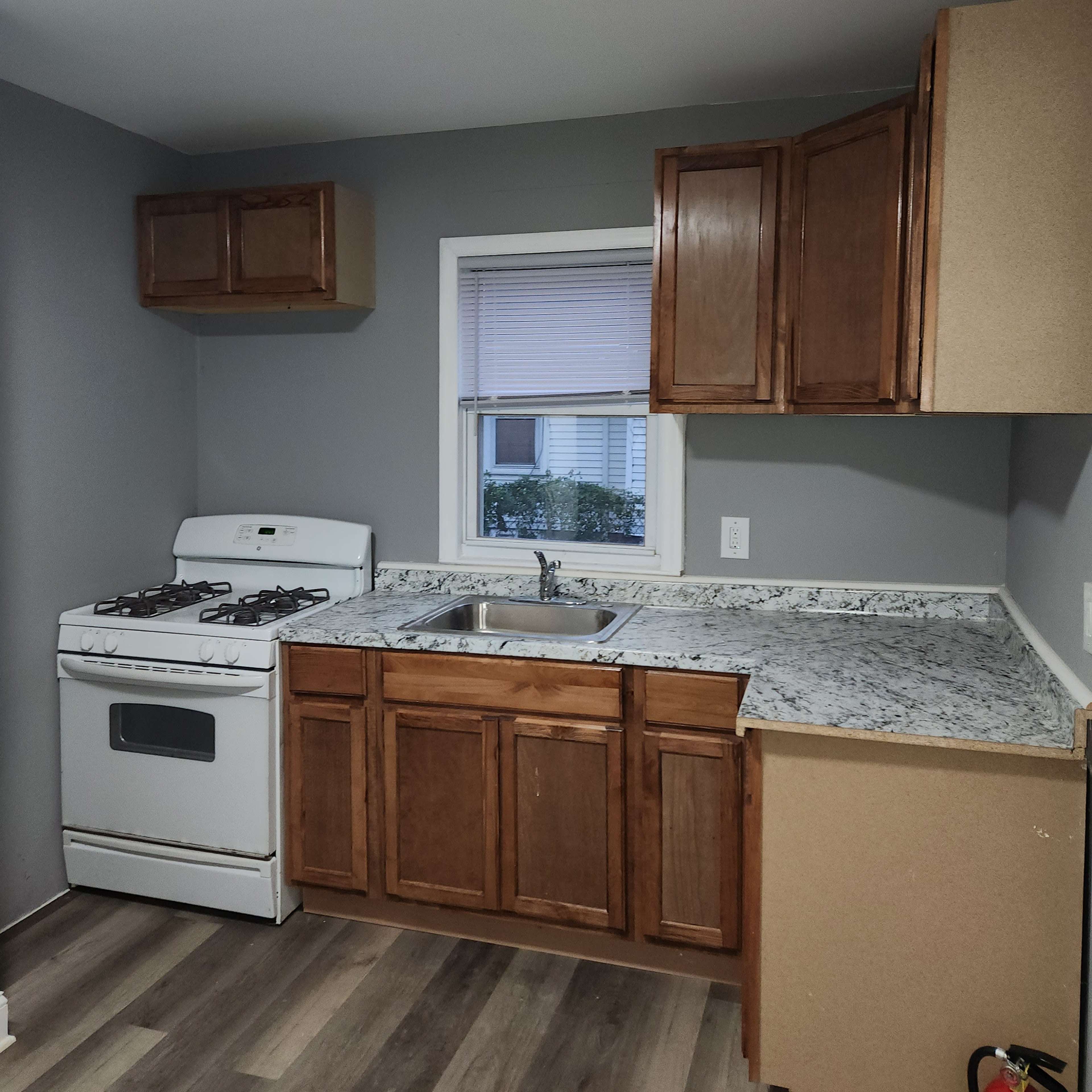 A kitchen featuring wooden cabinets, a countertop with a speckled finish, a white gas stove, and a window above the sink.