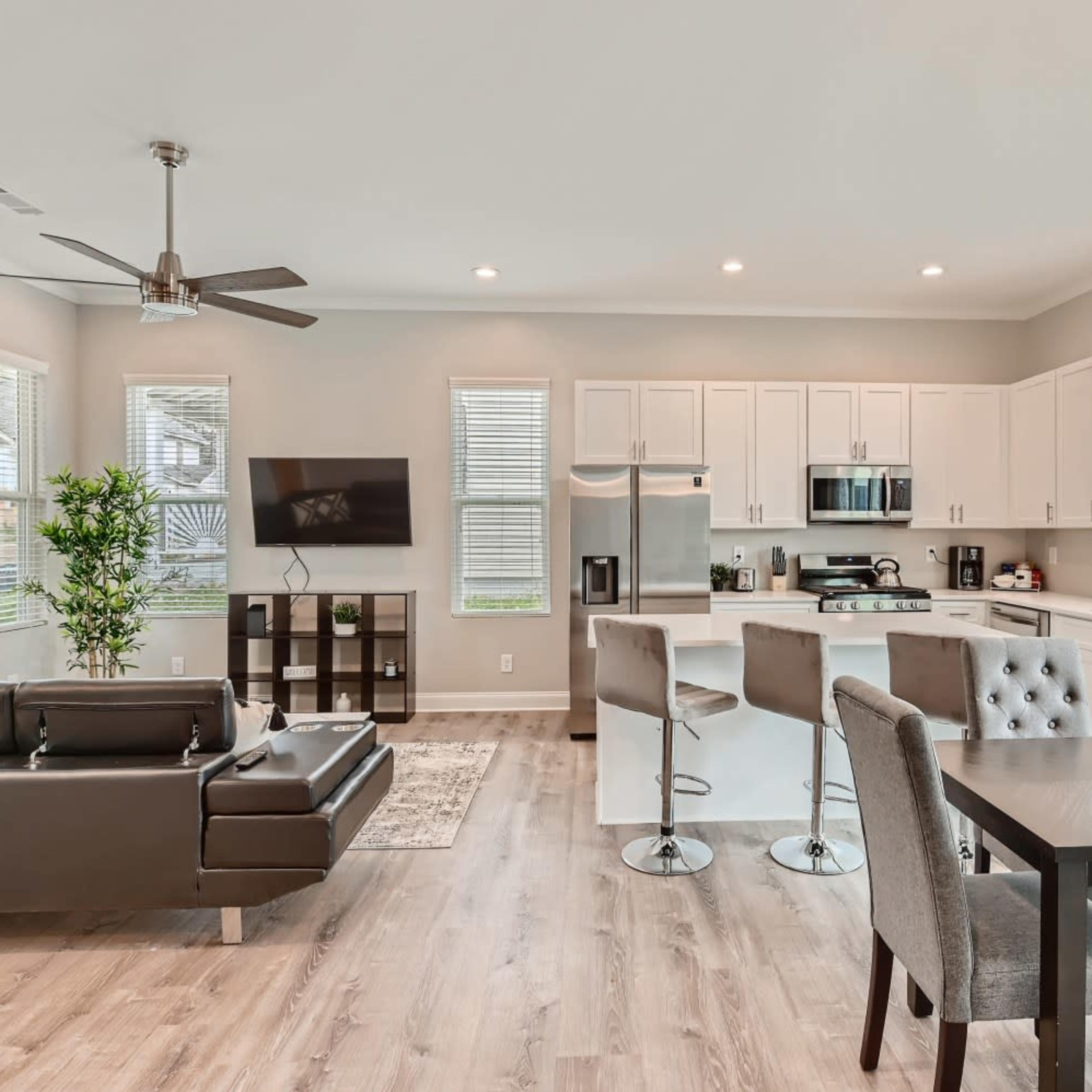A modern open-concept living space features a kitchen, dining area, and living room with sleek furnishings and large windows.