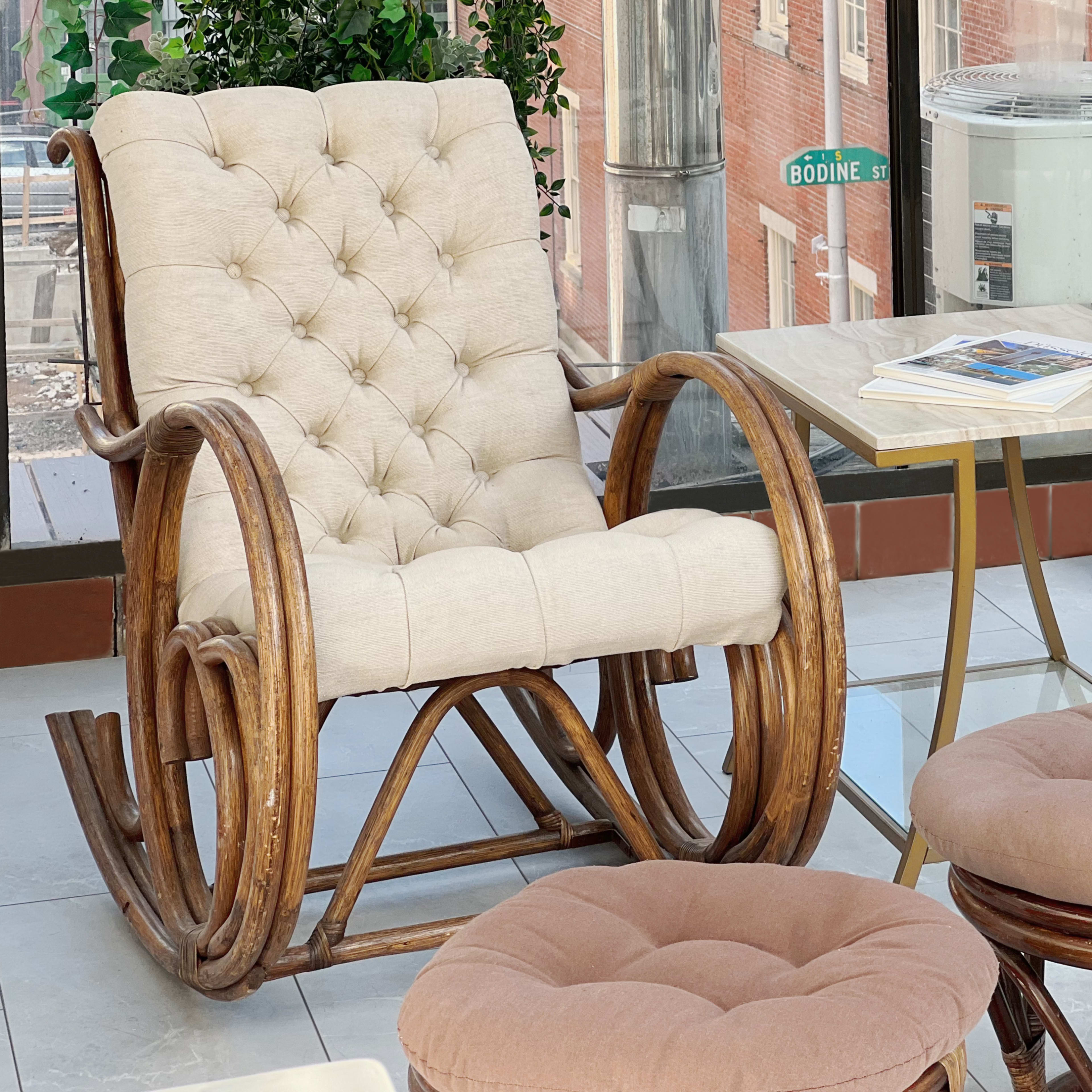 A rocking chair, a small table, and two cushioned stools arranged in a sunlit room with large windows.