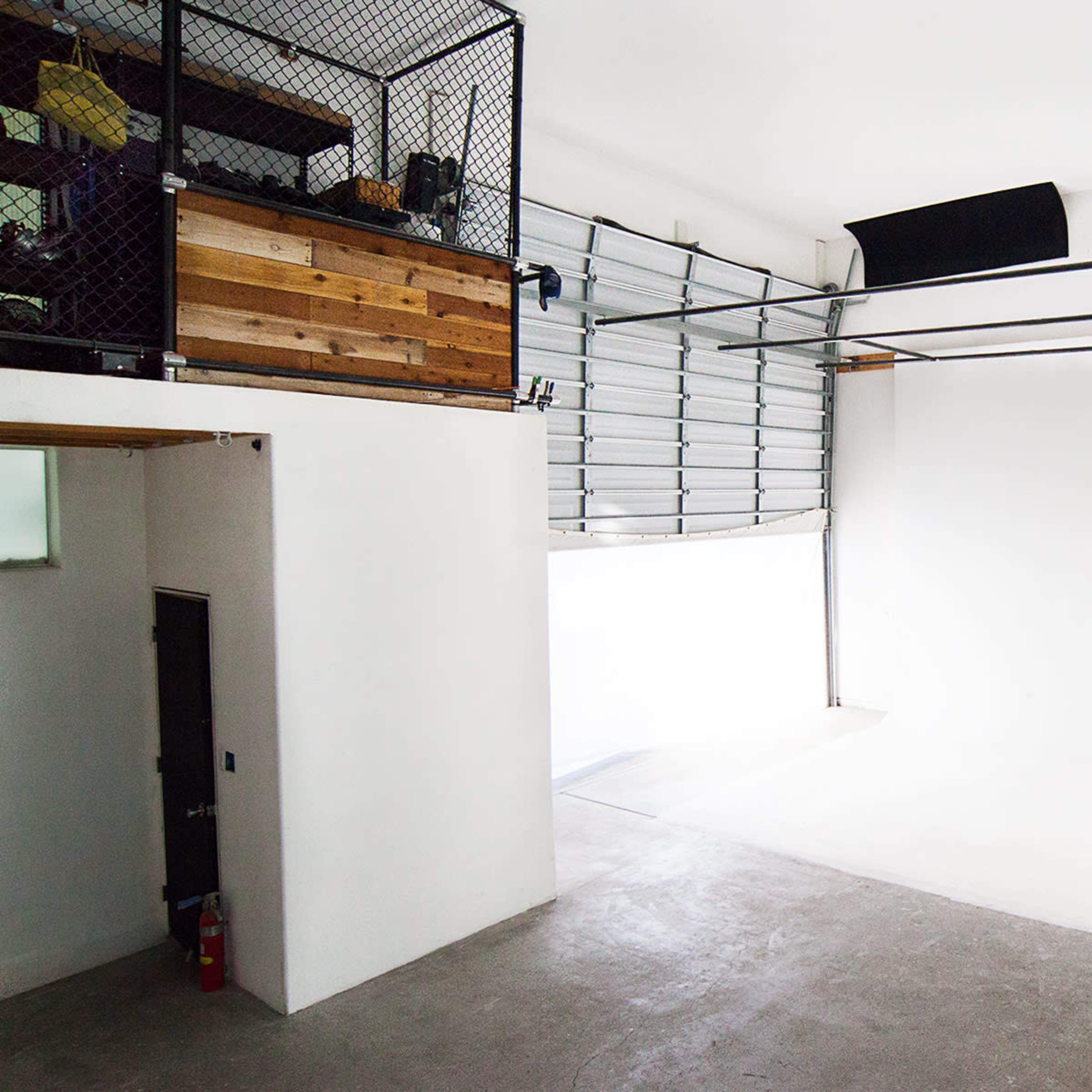 An empty industrial-style room with a high ceiling, a garage door, and a loft area with wooden elements.
