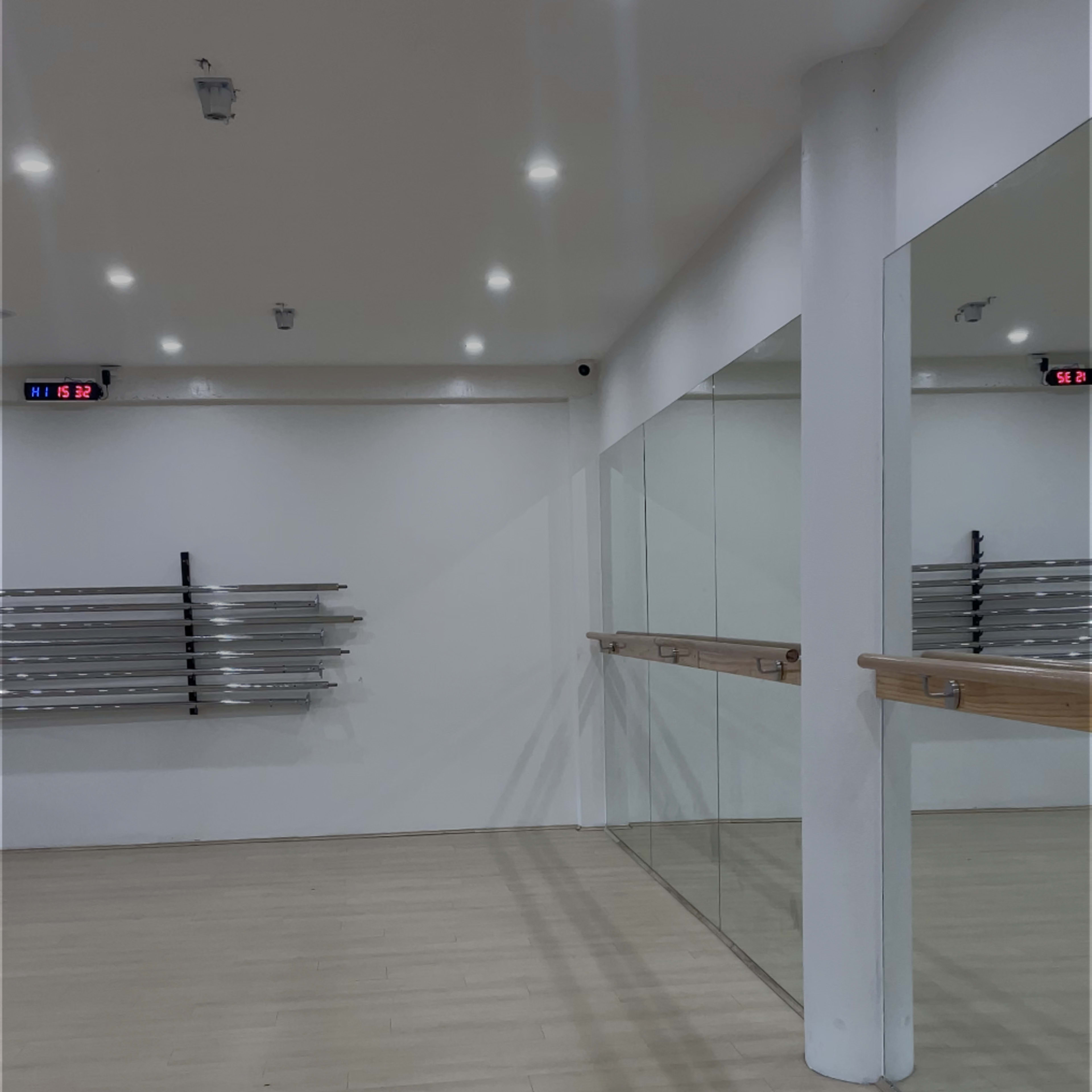 A spacious dance studio with wooden flooring, mirrored walls, and a barre along one side.