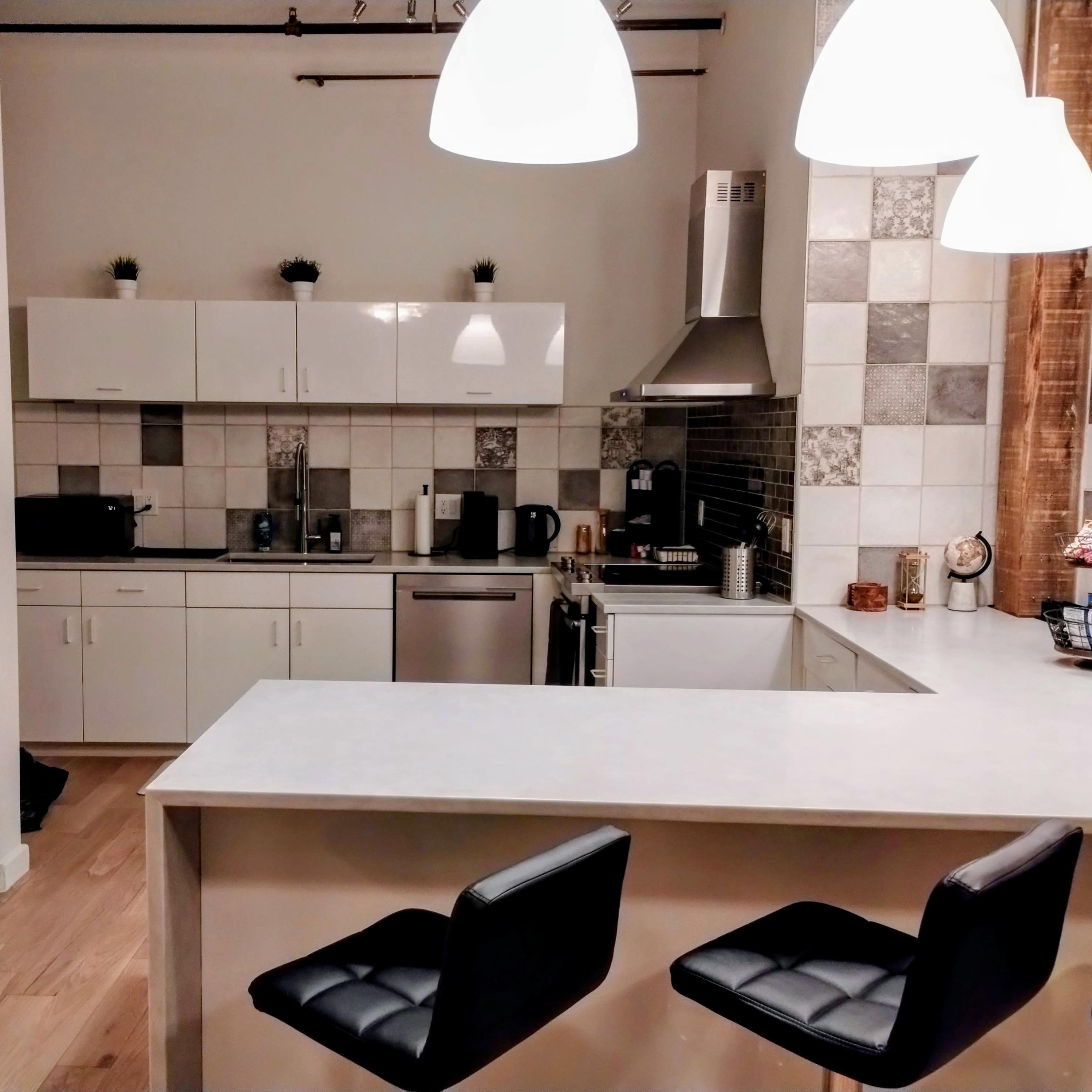 A modern kitchen with white cabinets, a silver refrigerator, and a bar area with black stools.