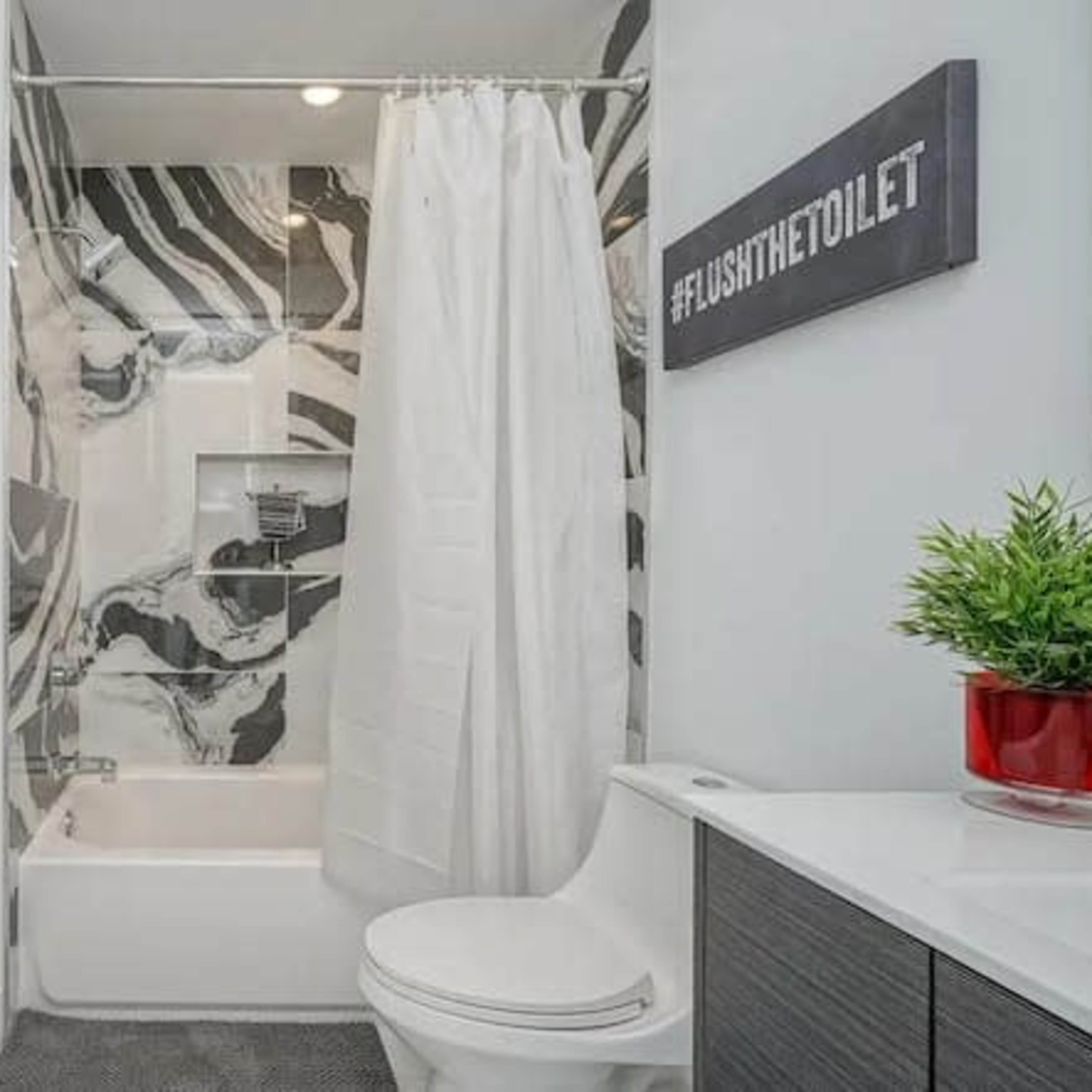 A modern bathroom featuring a bathtub with a shower curtain, a toilet, and abstract wall decor.