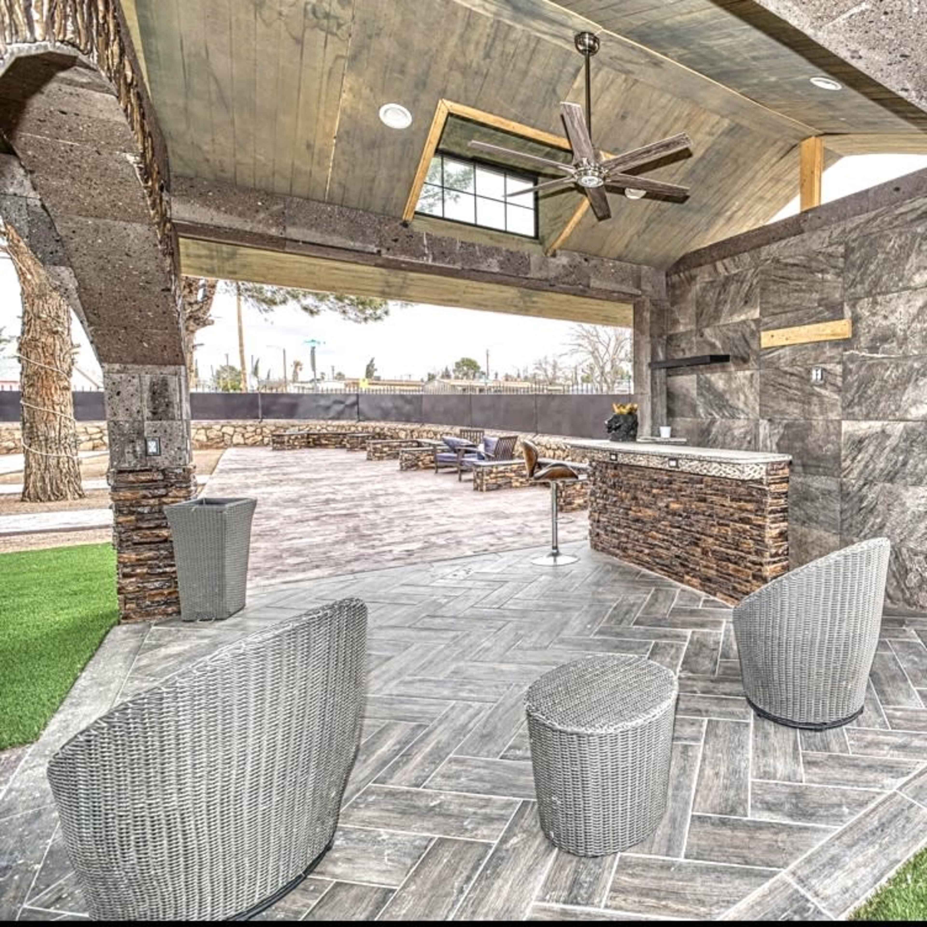 An outdoor patio area featuring a stone bar with seating, surrounded by landscaped grass and a covered roof.