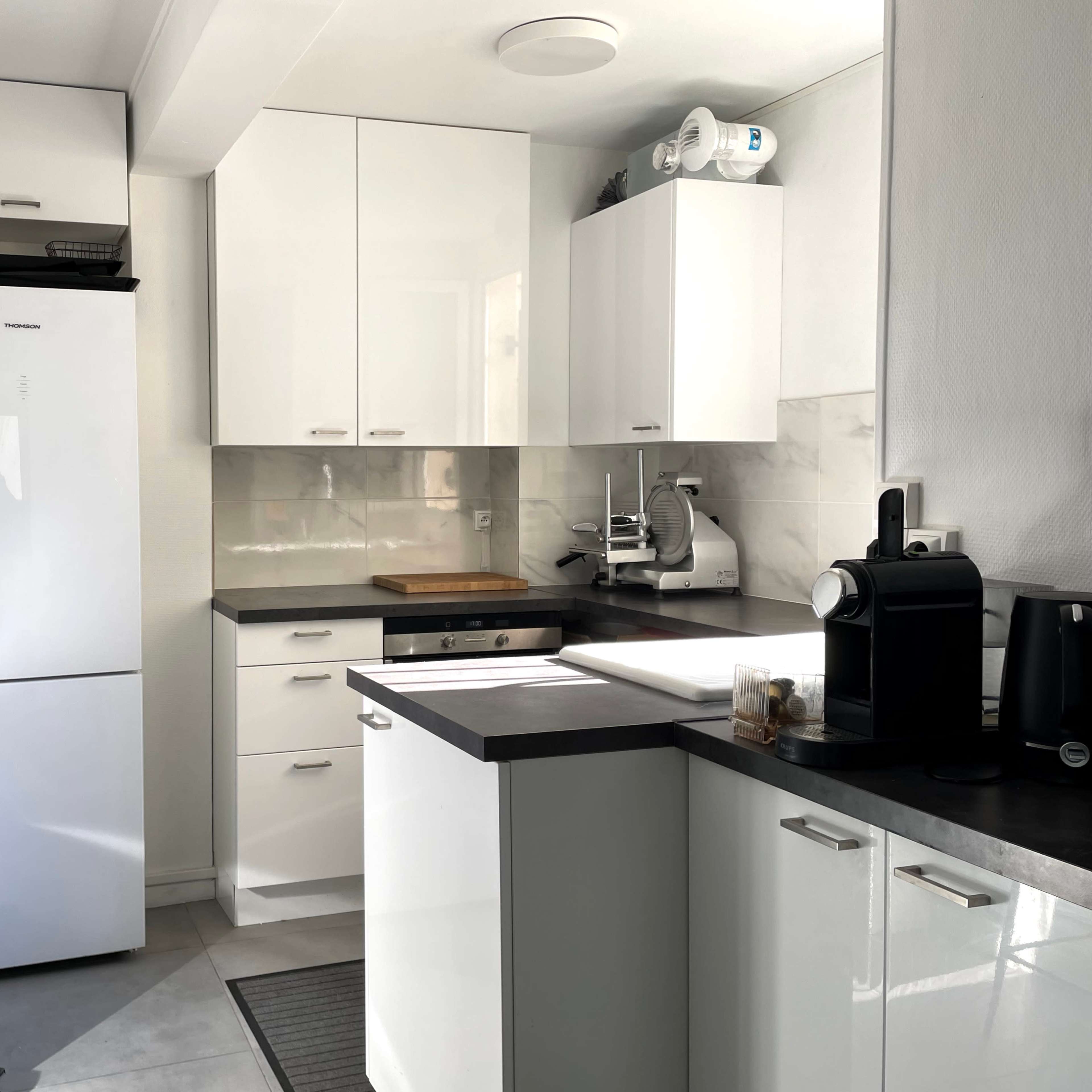 A modern kitchen with white cabinets, a refrigerator, and various appliances on a countertop.