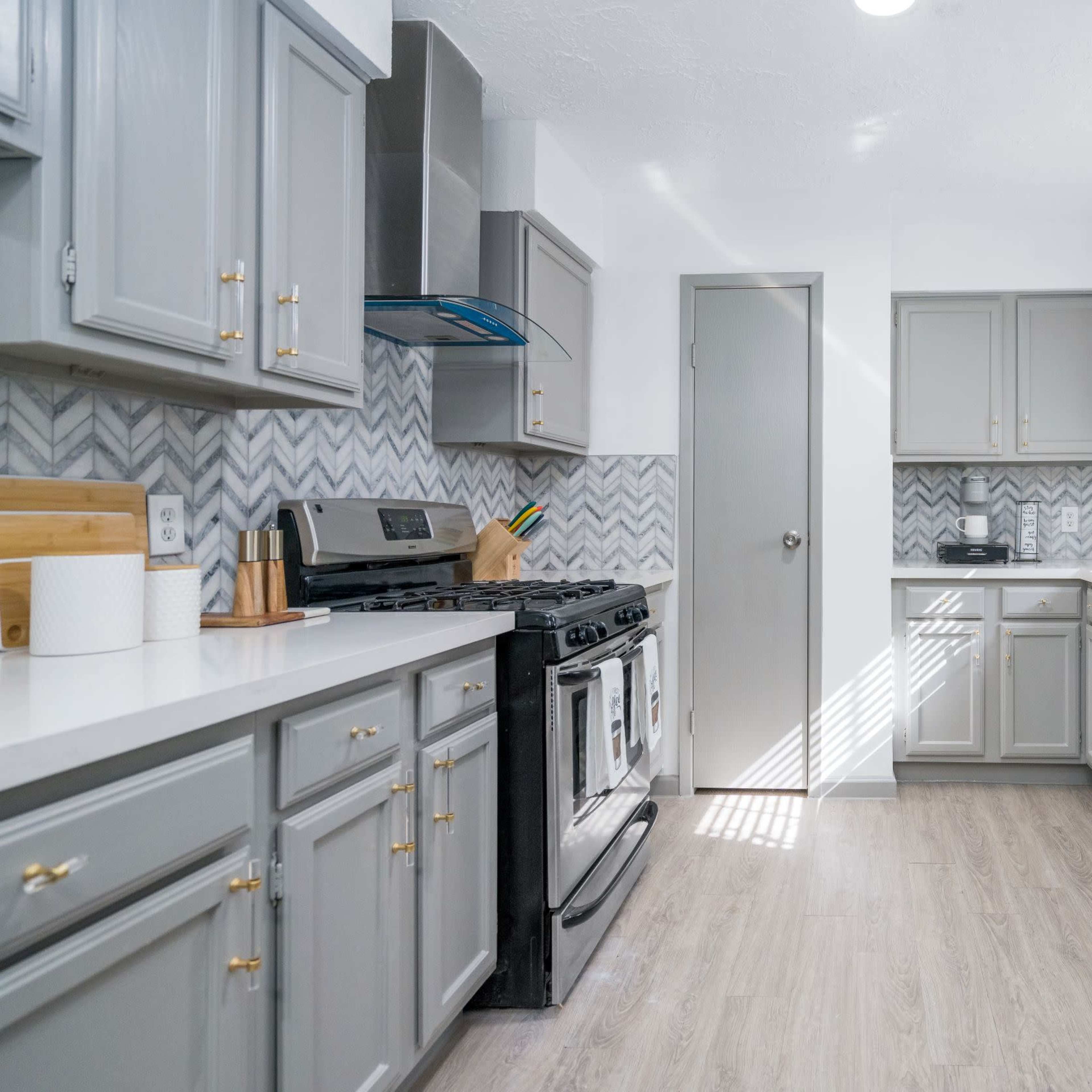 A modern kitchen features gray cabinets, a stainless steel refrigerator, and a gas stove, with natural light coming through a window.