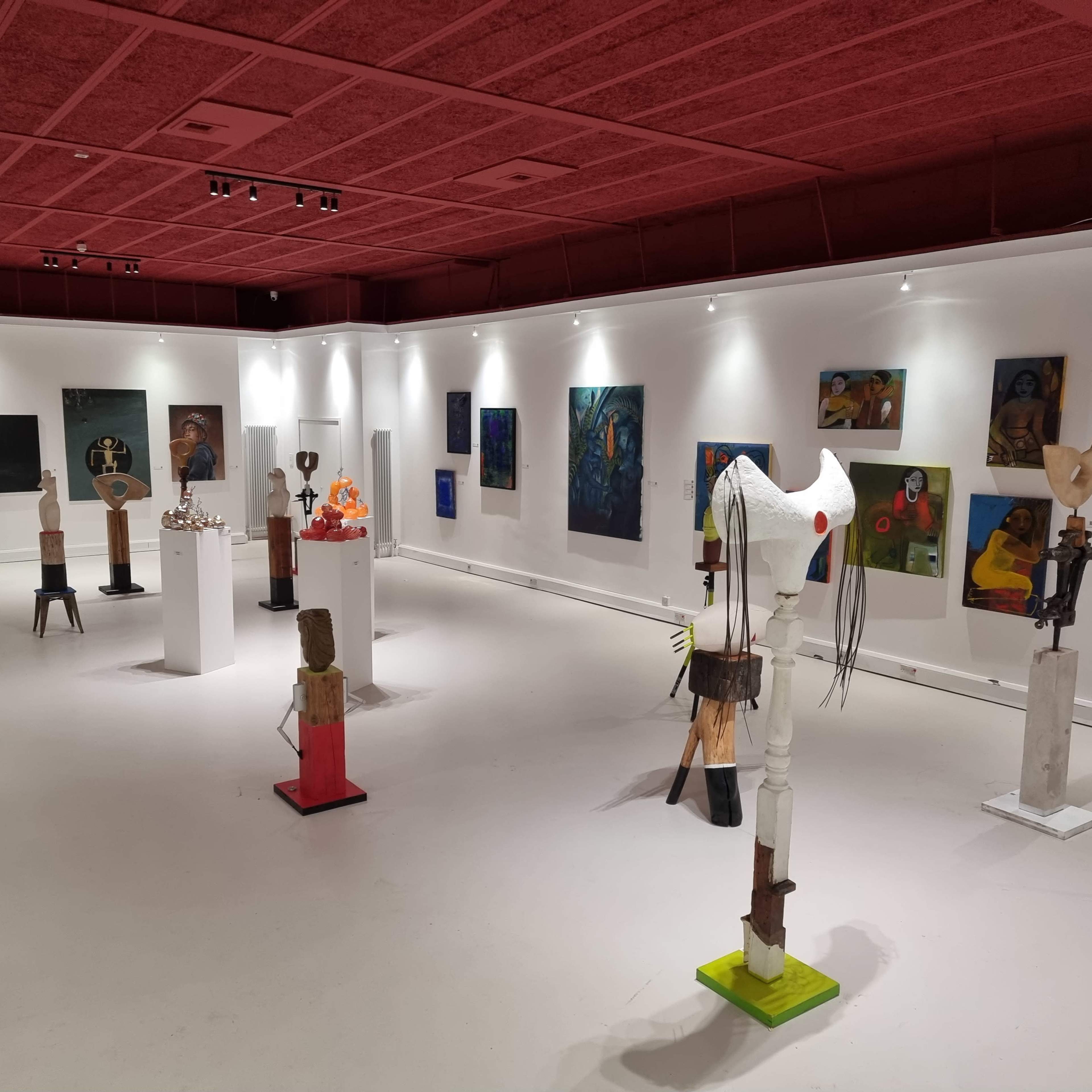 An art gallery featuring various sculptures and paintings displayed on white walls and pedestals.