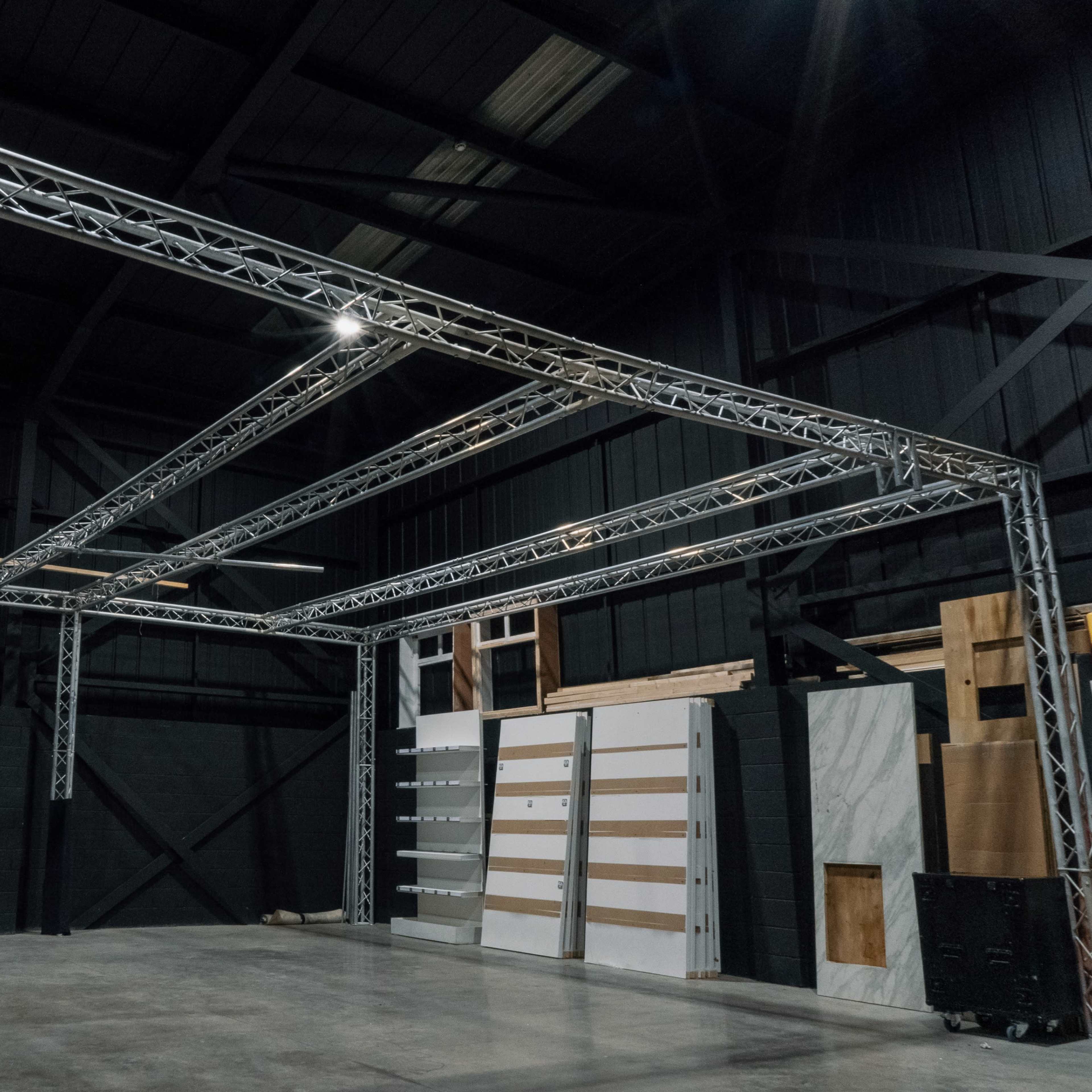 A spacious industrial interior with a metallic truss structure overhead and various panels against the walls.