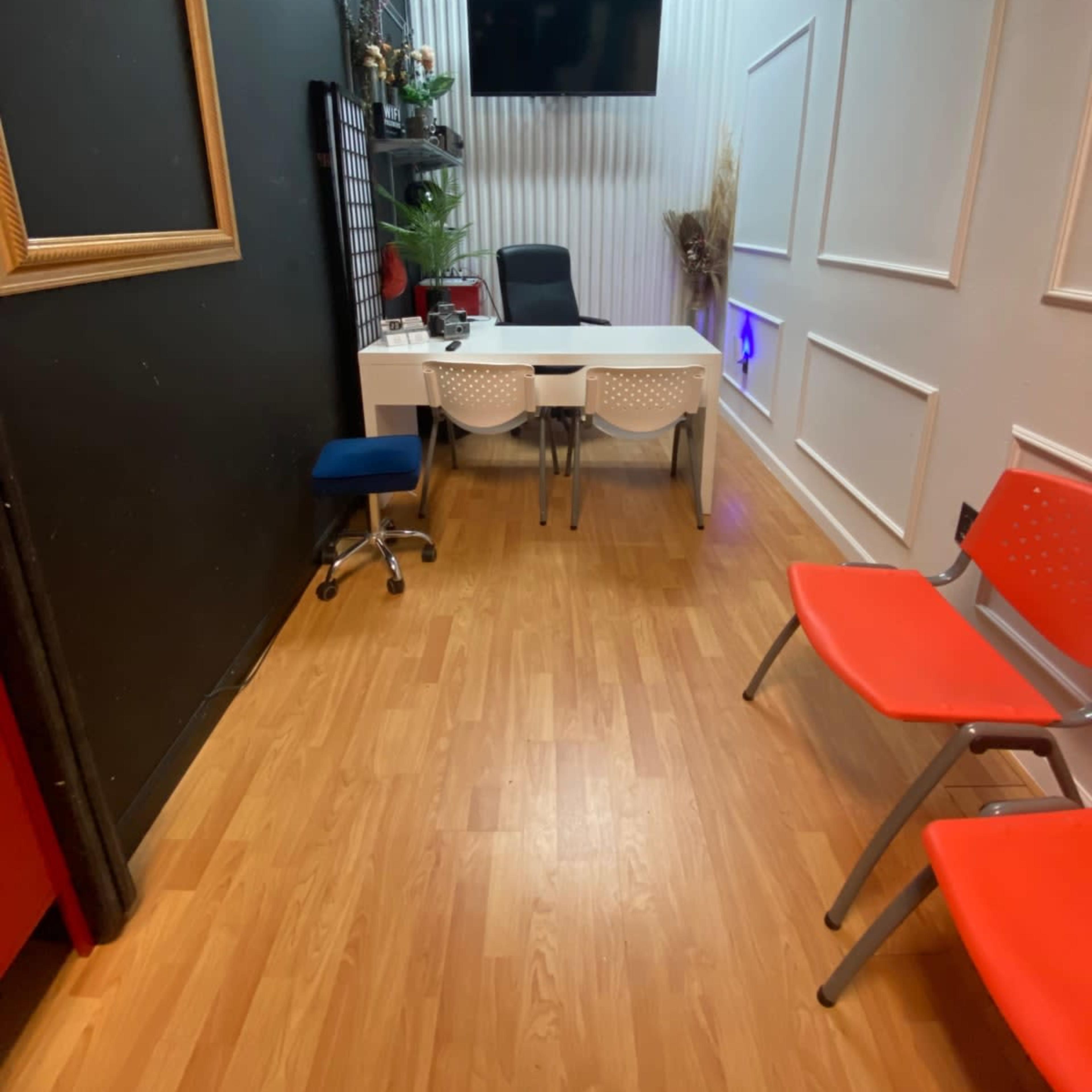 A small office space with a desk and chairs, wooden flooring, and a wall-mounted TV.