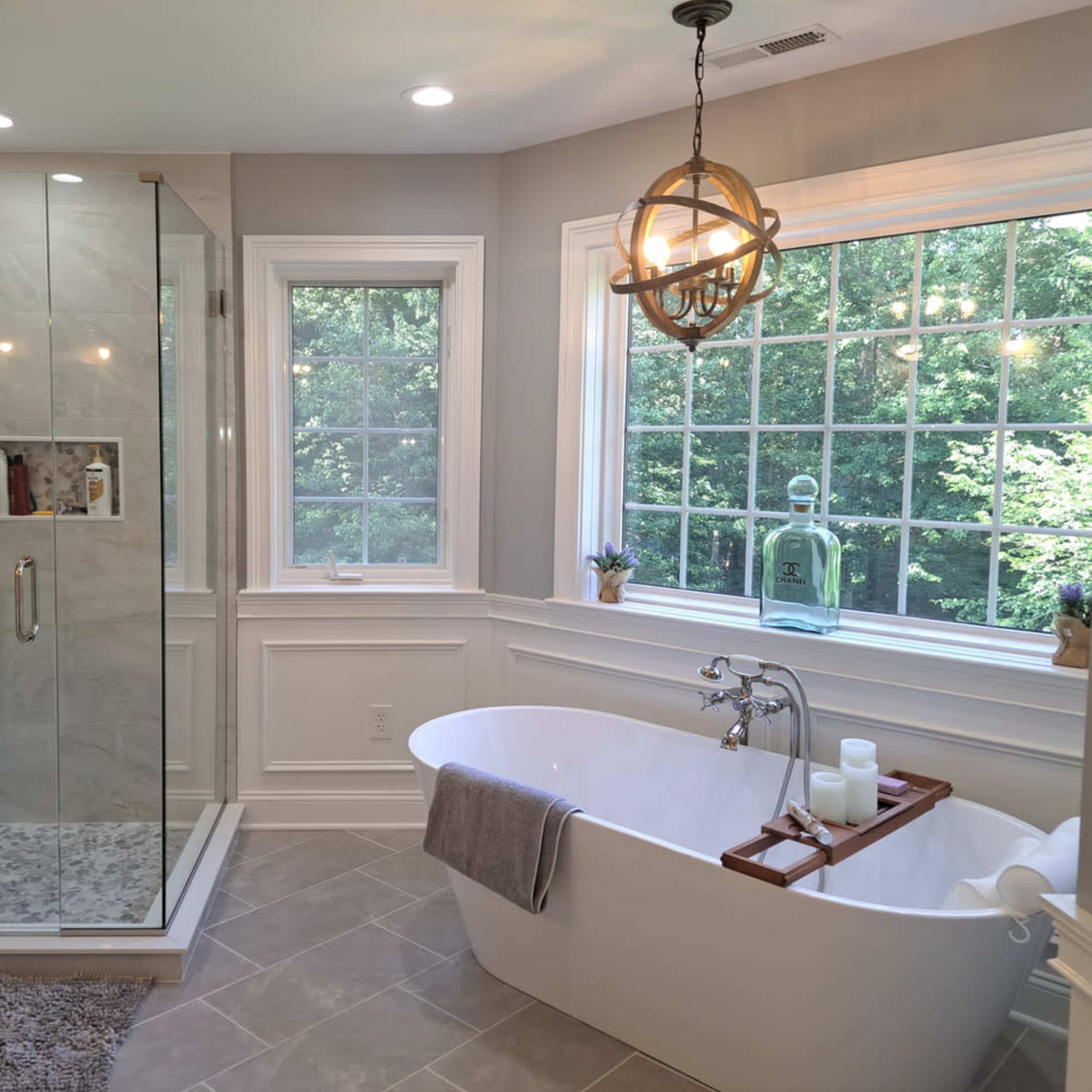 A modern bathroom featuring a glass shower enclosure, a freestanding bathtub, and a large window providing natural light.