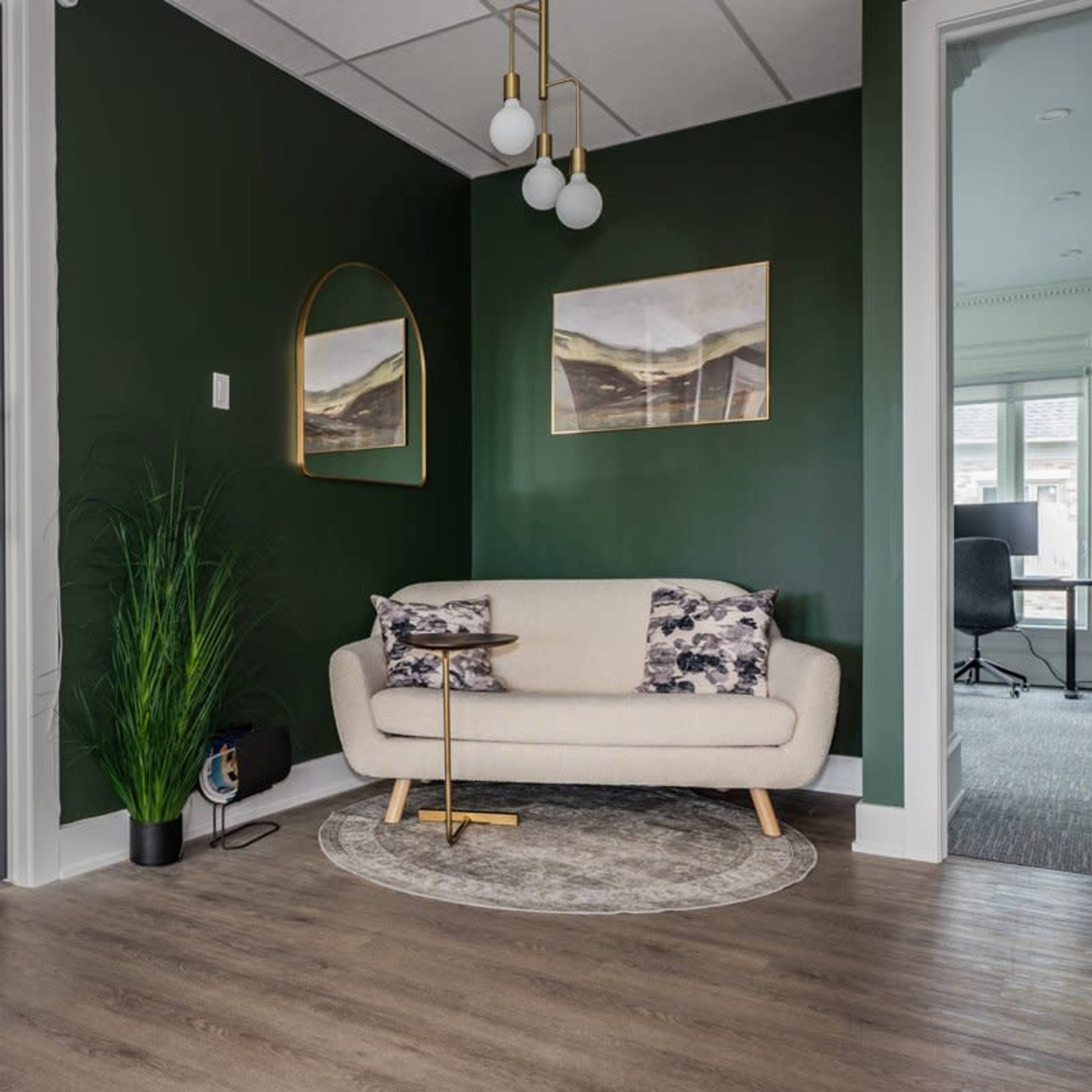 A cozy entryway featuring a green accent wall, a light-colored sofa with patterned cushions, and modern artwork, complemented by a plant and a round rug.