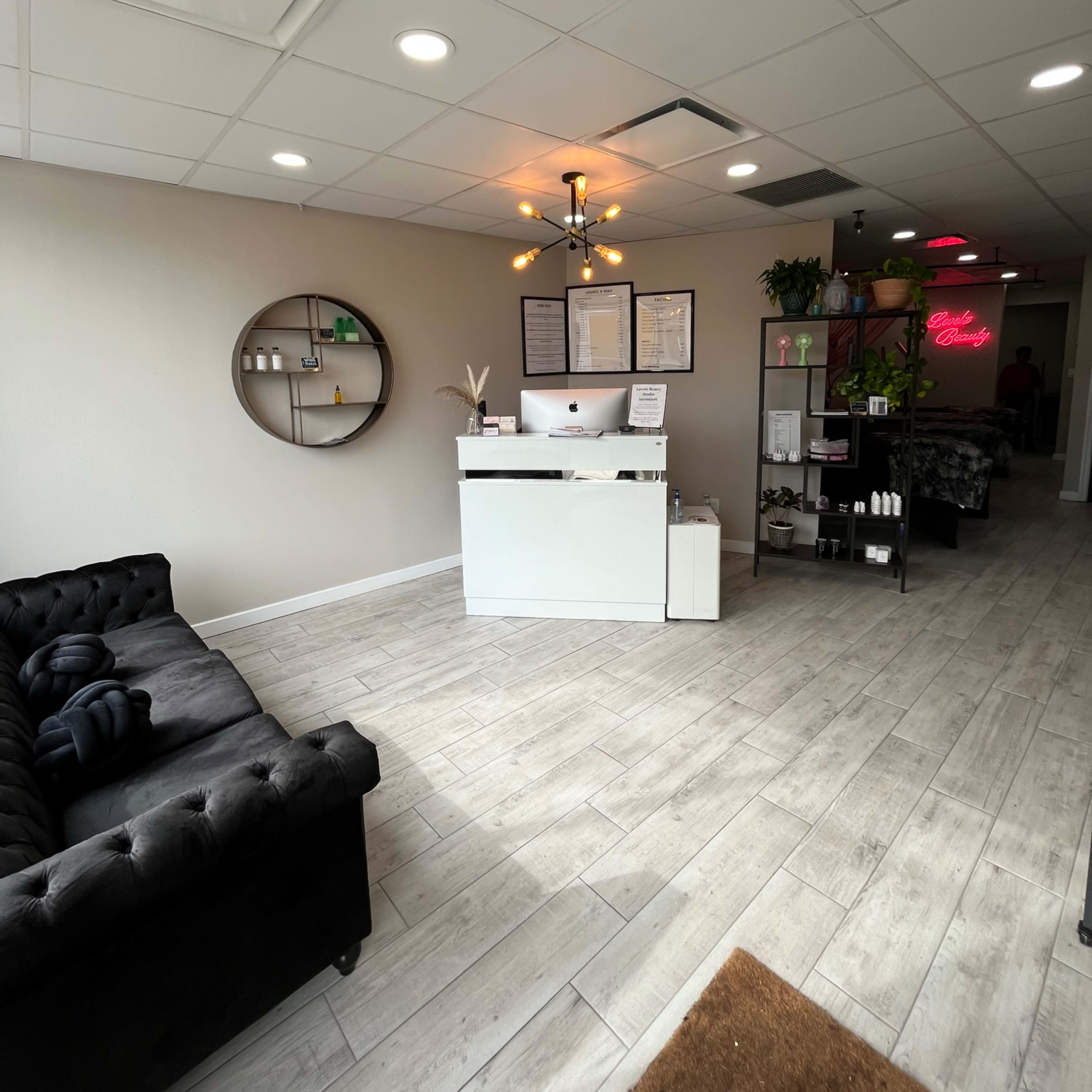 A modern reception area with a white front desk, a black tufted sofa, and various decorative items arranged on the walls and shelves.
